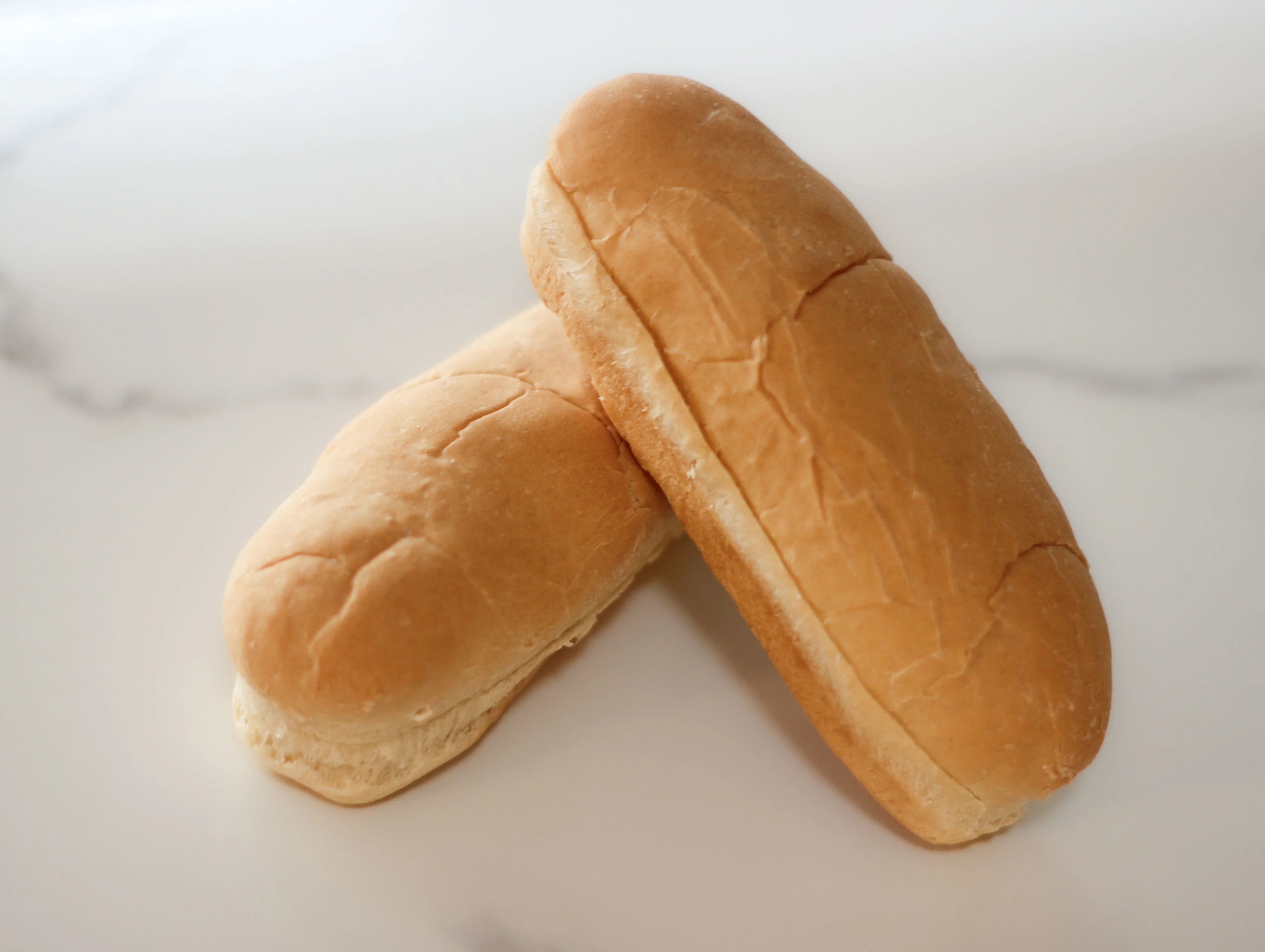 Two soft bread rolls stacked on a marble surface.
