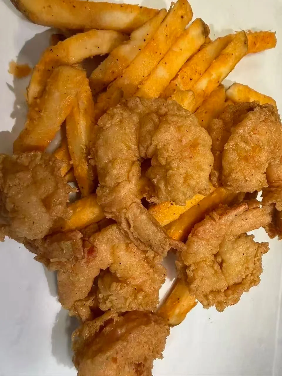 A plate of crispy fried shrimp accompanied by seasoned French fries, appealingly arranged.