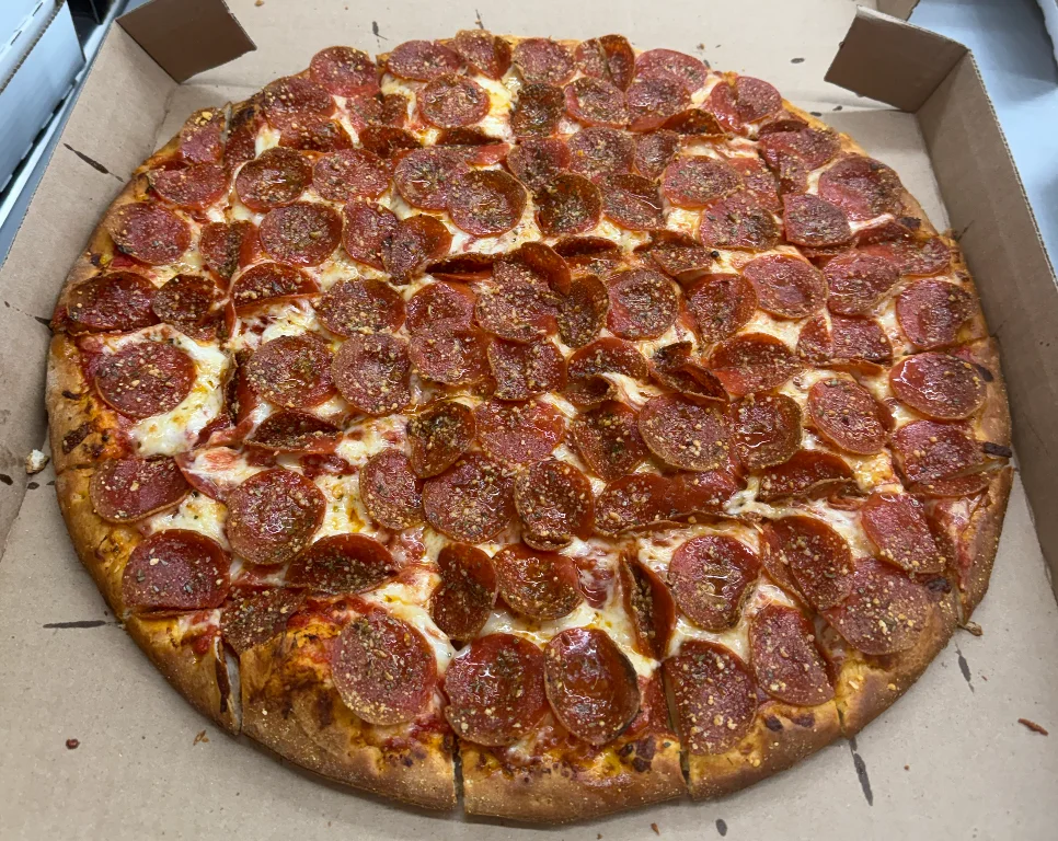 A large pepperoni pizza with slices evenly distributed. The pizza is topped with a generous amount of crispy pepperoni and is presented in its cardboard box.
