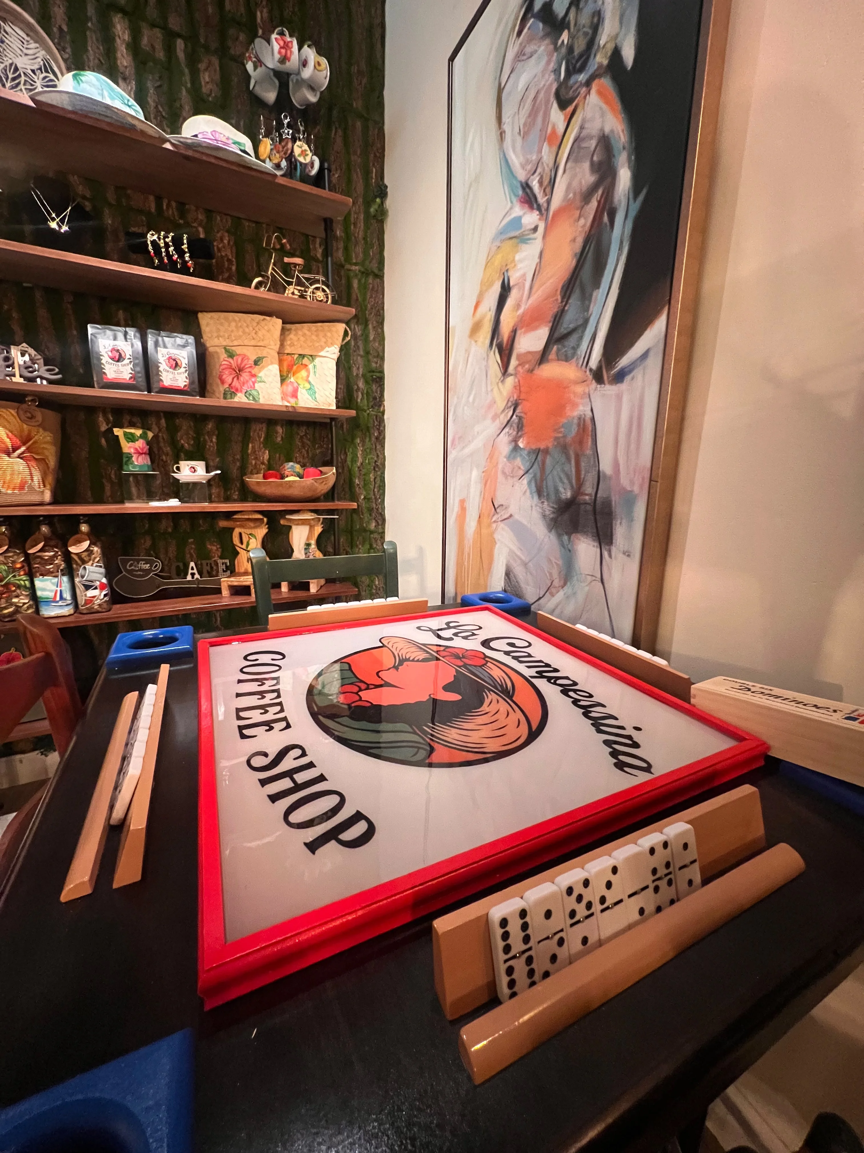 A cozy coffee shop display featuring a prominent sign and a variety of decorative items on shelves, including traditional crafts and a colorful painting.