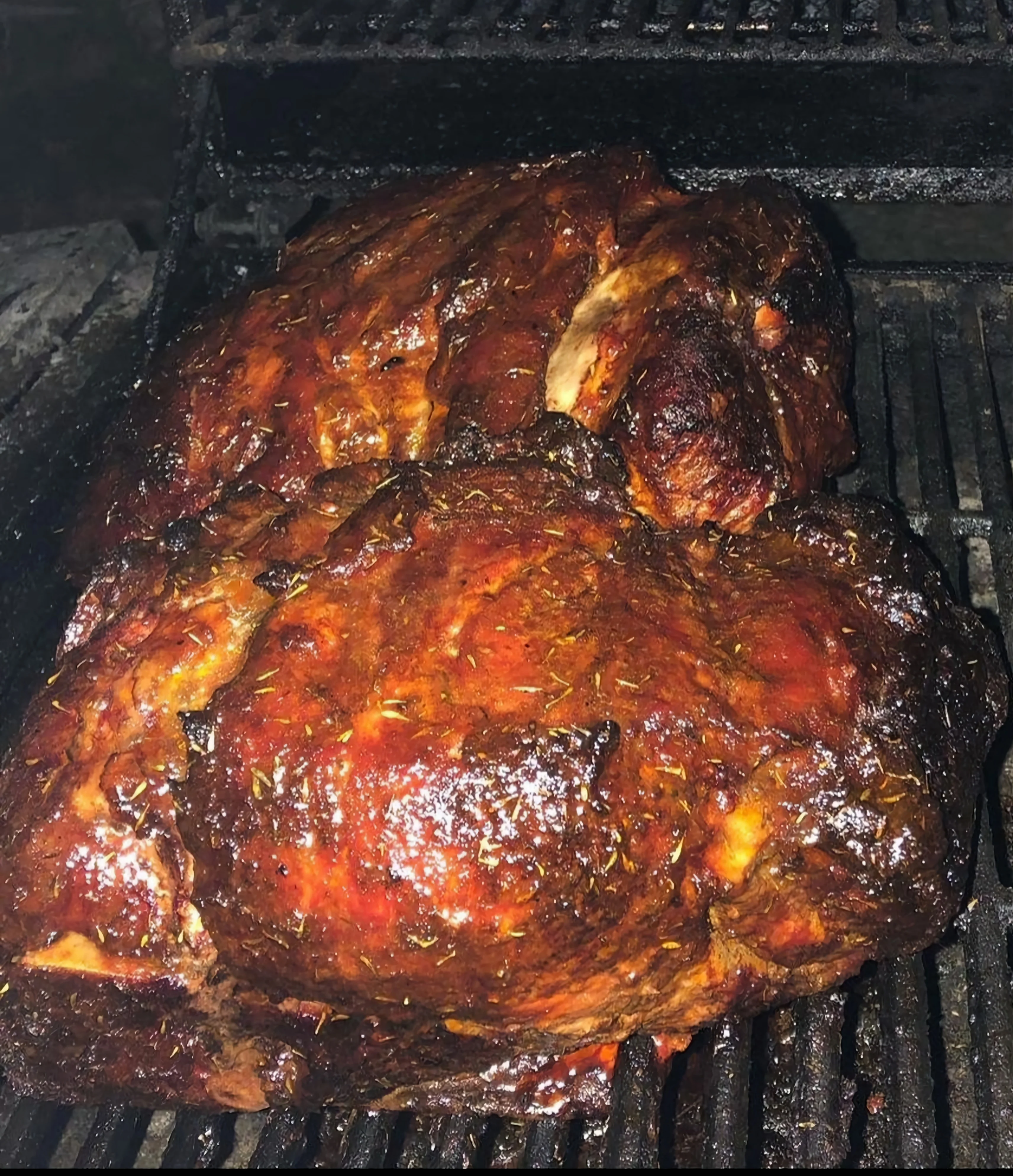 A large piece of smoked meat on a grill, with a shiny, glazed surface.
