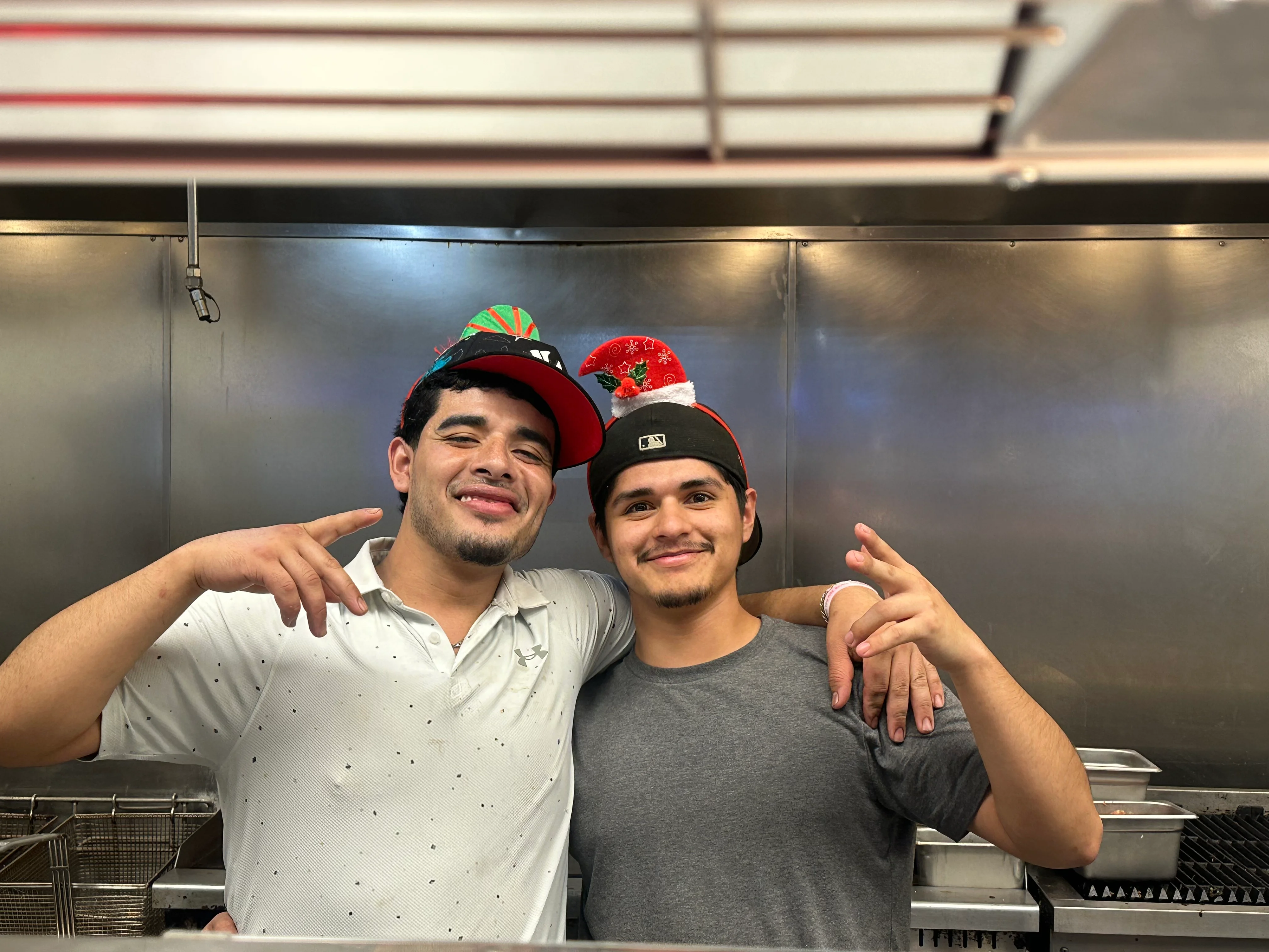 Two chefs smiling in a restaurant kitchen wearing festive hats