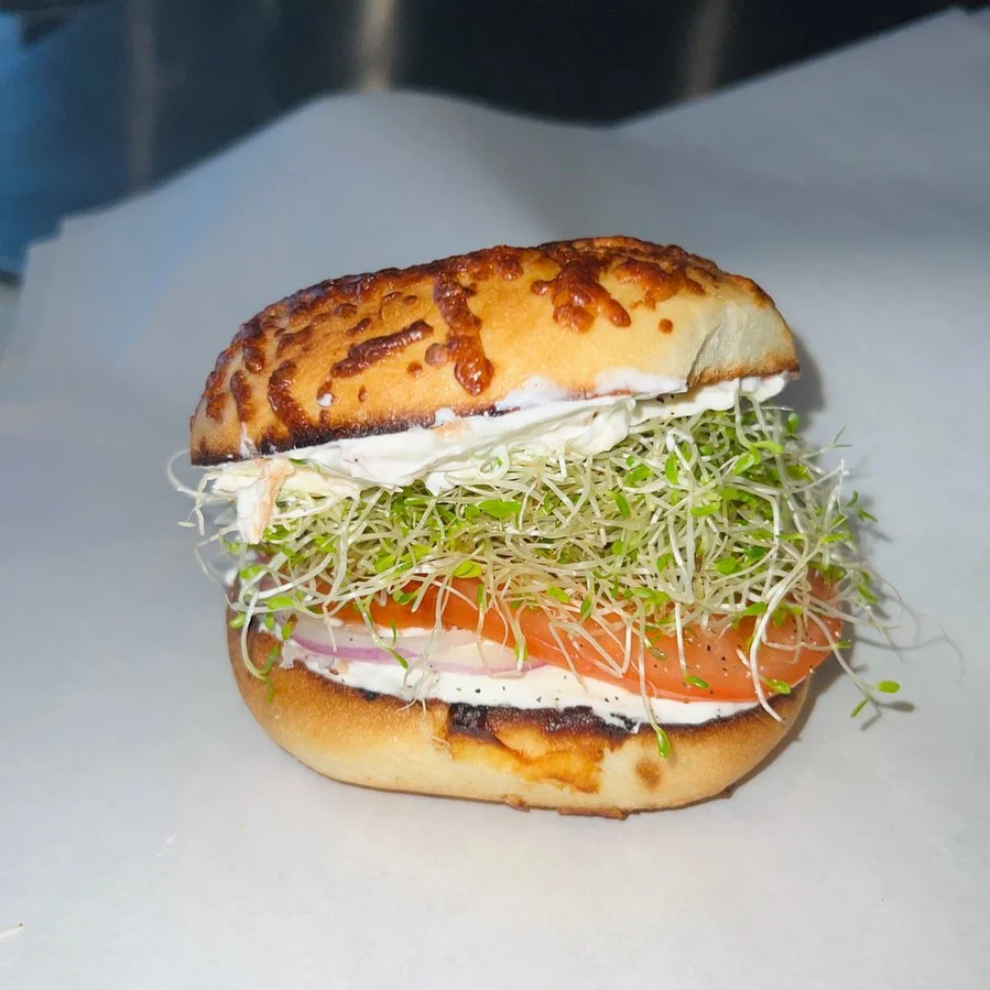 A delicious sandwich featuring a toasted bun filled with layers of tomato, sprouts, and mayonnaise.