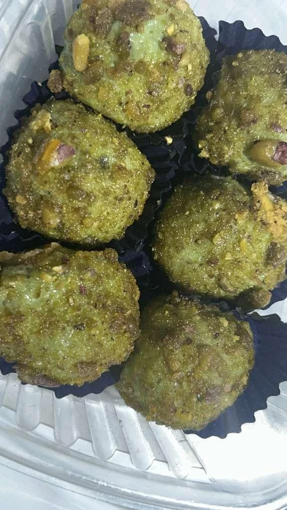 A close-up view of several green sweets, possibly made with pistachios, arranged neatly in individual paper cups.