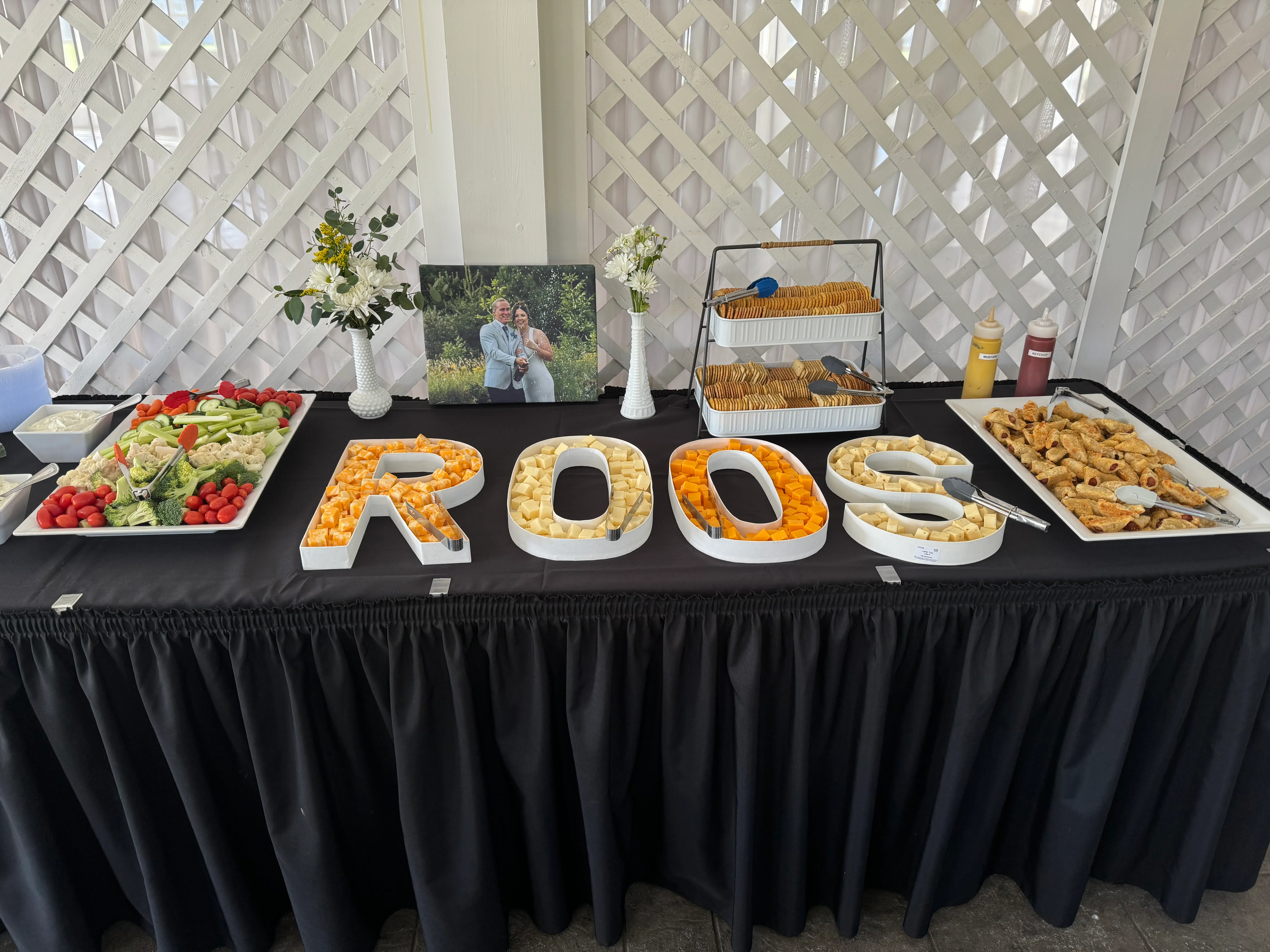 A buffet table with assorted food arranged in letter shapes and a photo backdrop.