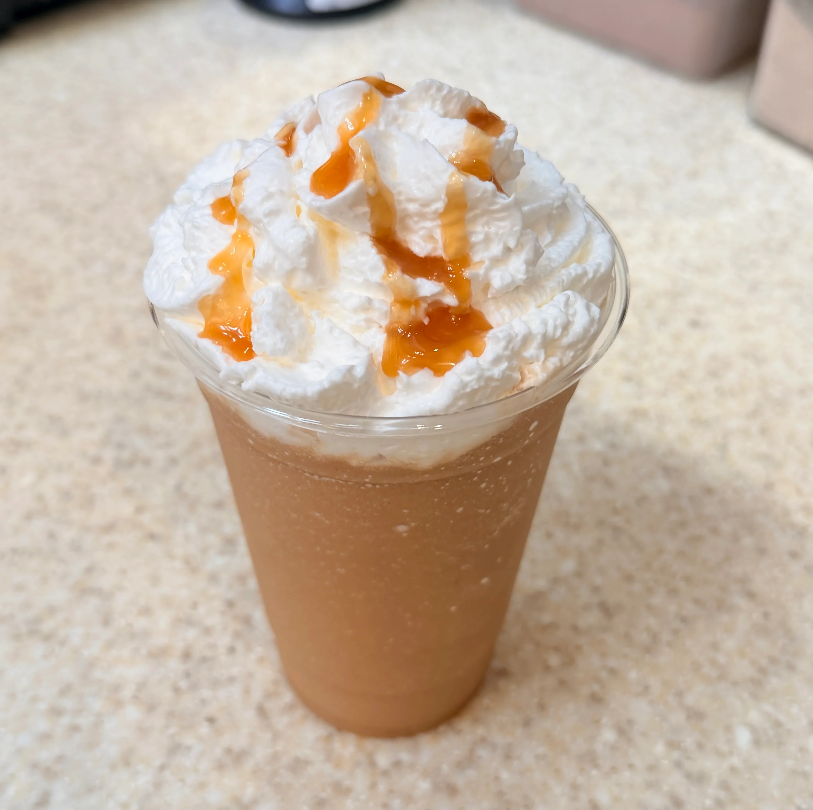 Frosted caramel drink topped with whipped cream and caramel drizzle.
