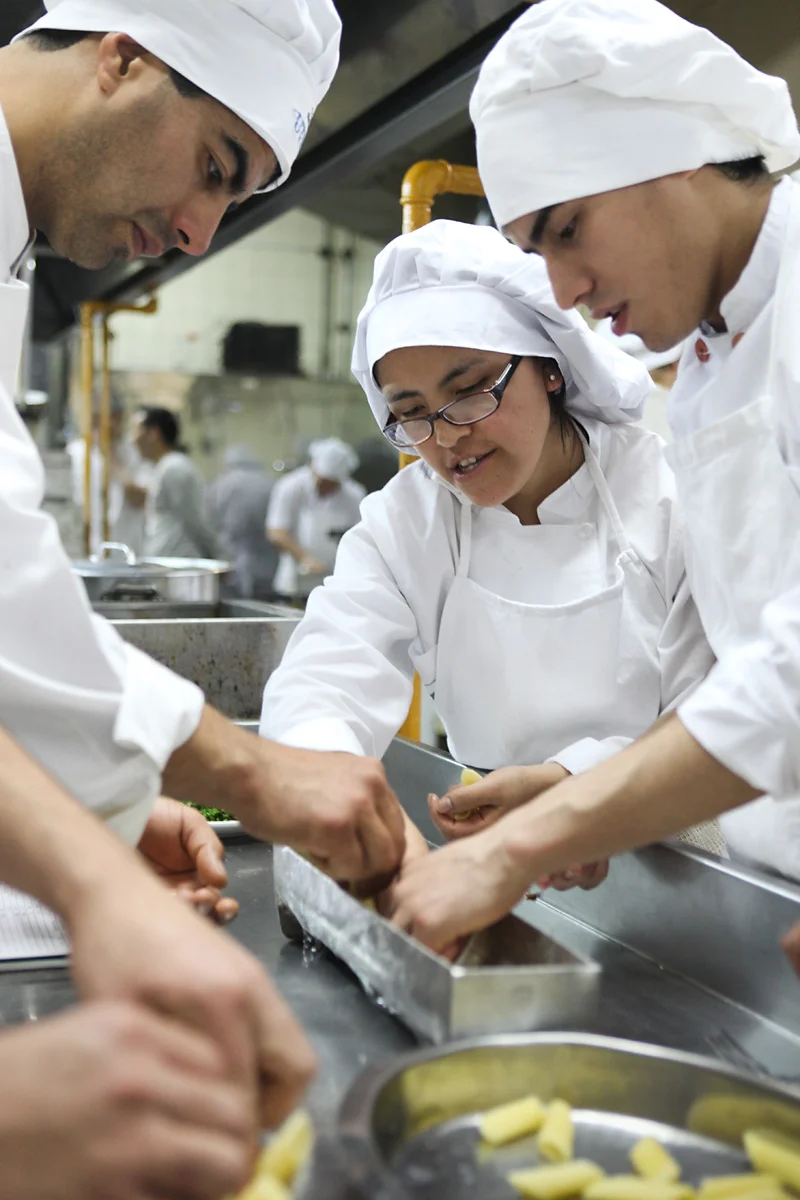 Culinary students collaborating in a kitchen, preparing pasta.