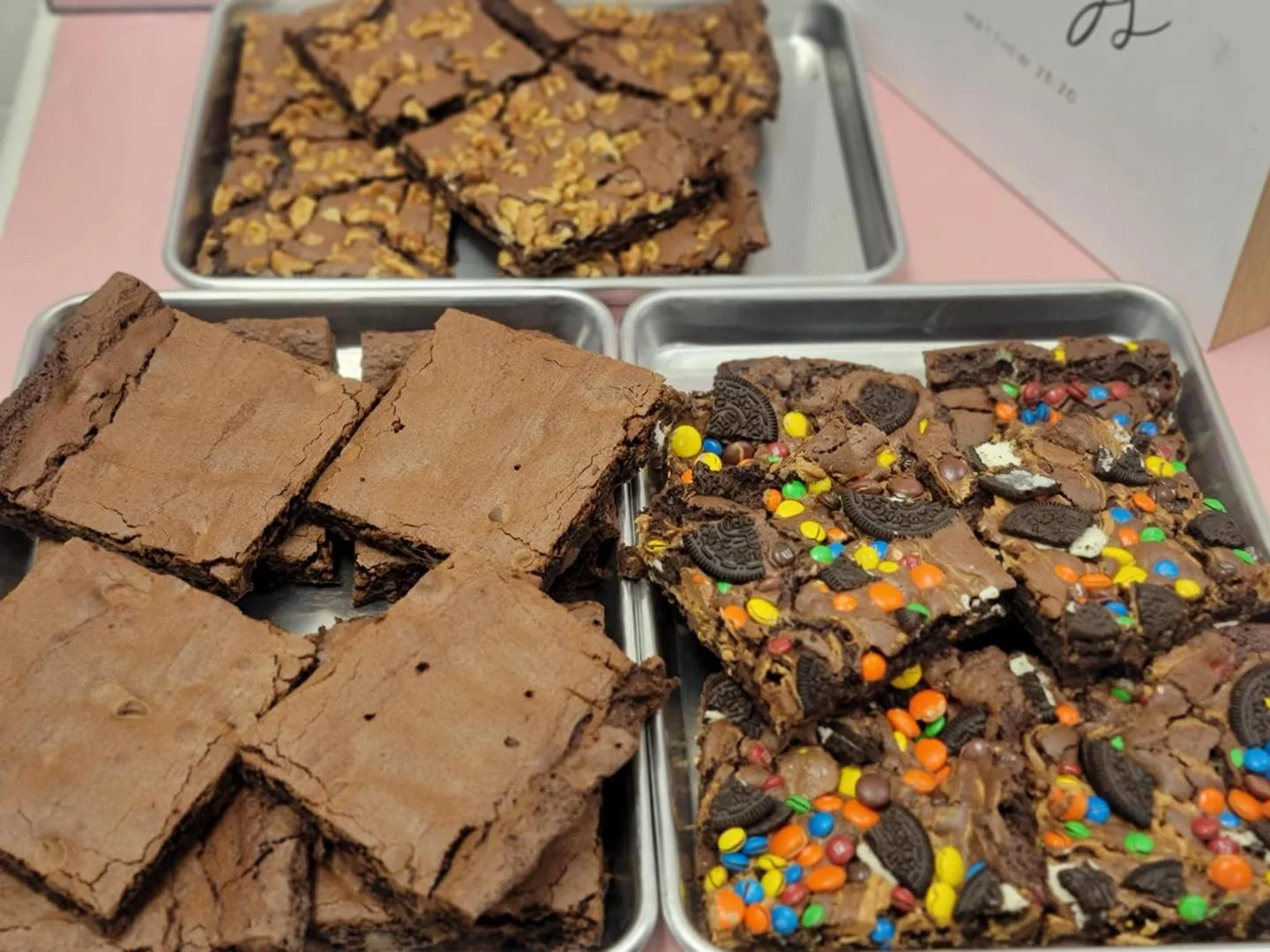 Trays of brownies, some topped with nuts, others with colorful candies and Oreo pieces.