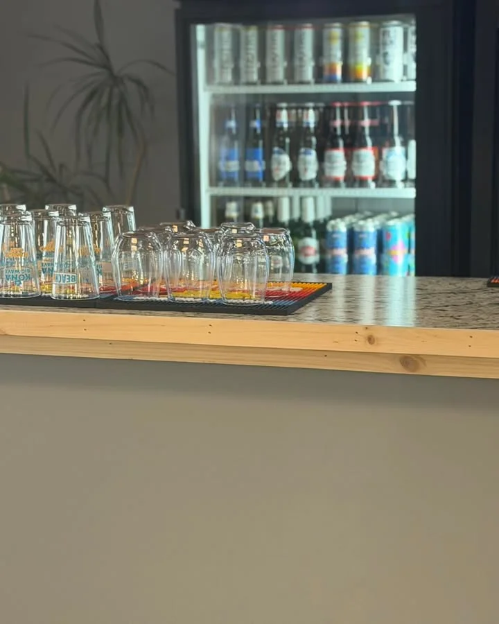 A bar counter displaying several stacked glasses and a refrigerating unit filled with assorted beverages.