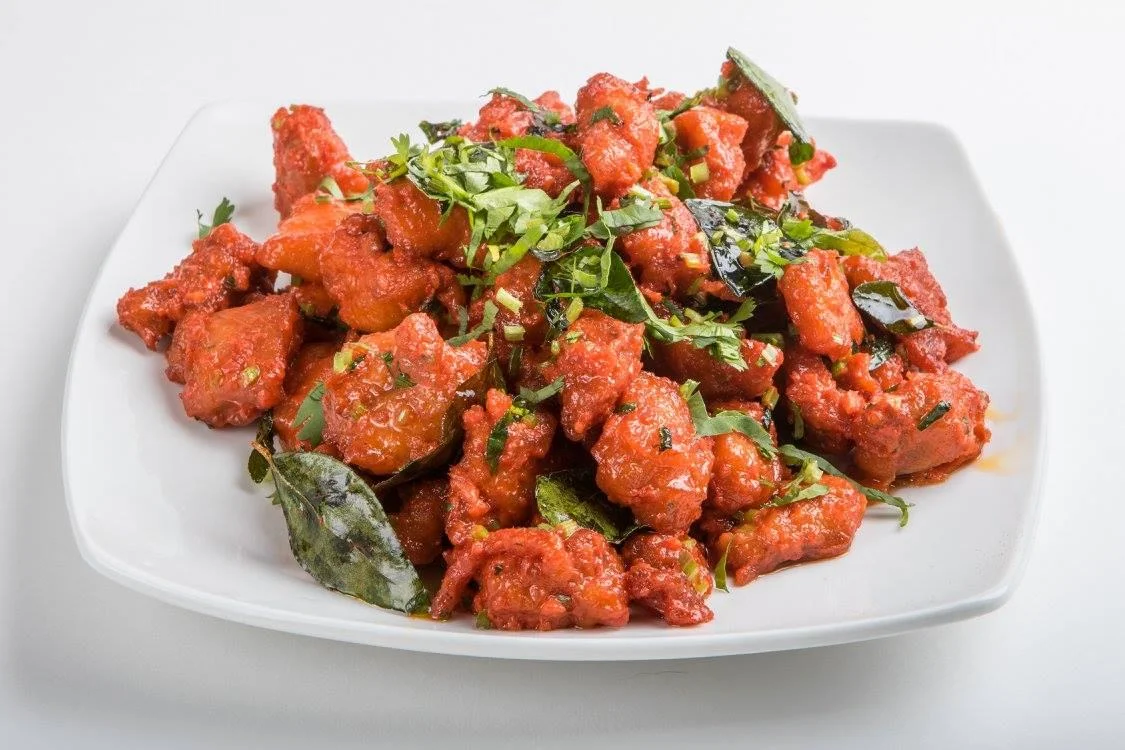 A vibrant dish of deep-fried pieces mixed with herbs and spices, garnished with greens.