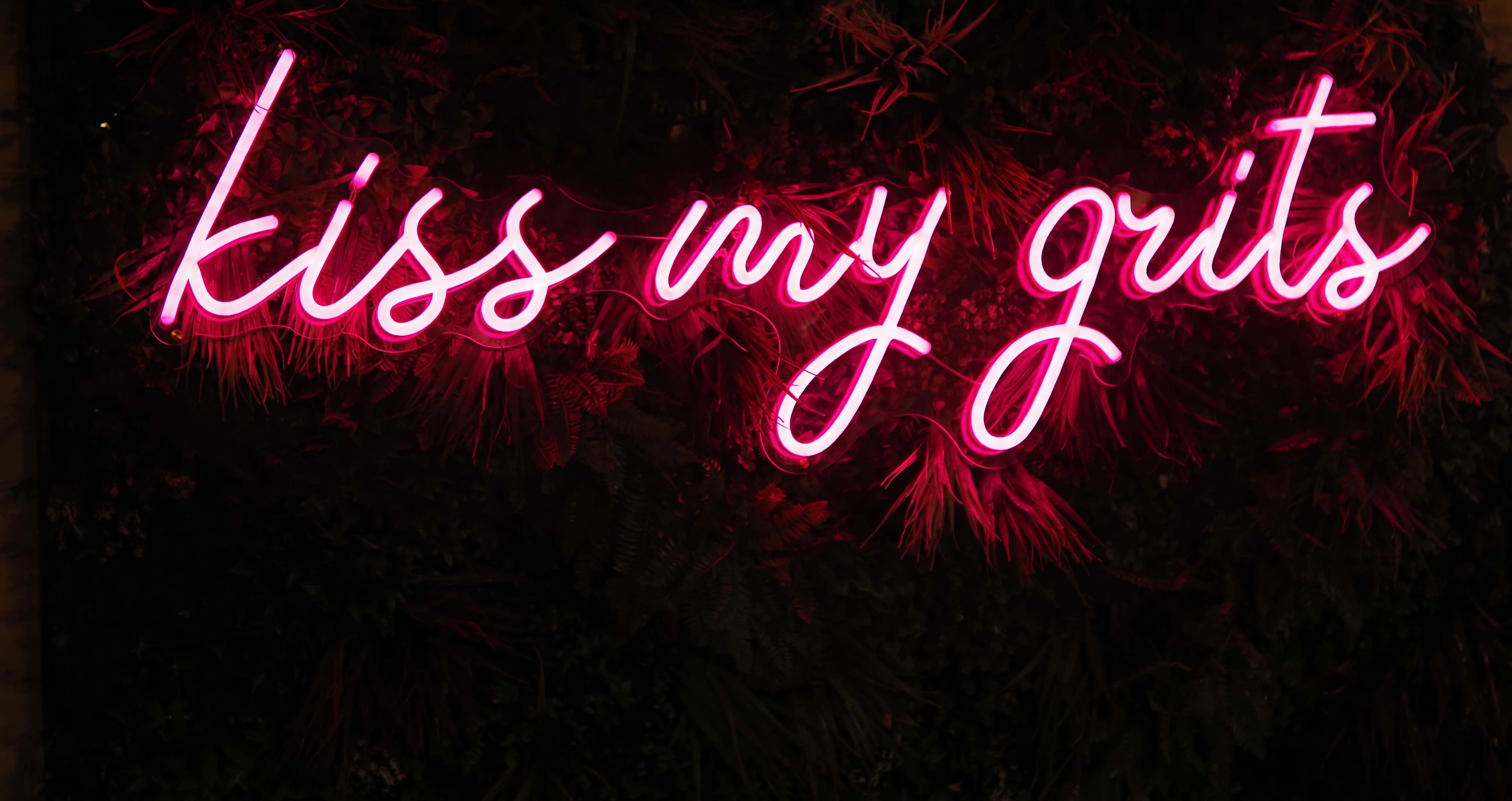 Neon sign reading 'kiss my grits' in a cozy restaurant setting
