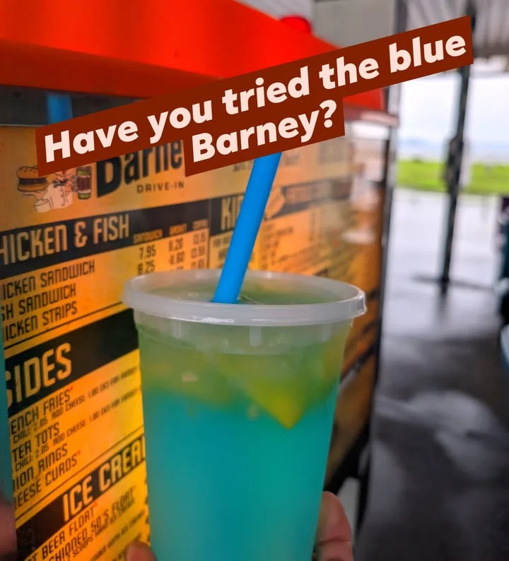 A colorful drink resting on a counter, with a straw and slices of lemon, in front of a menu board.