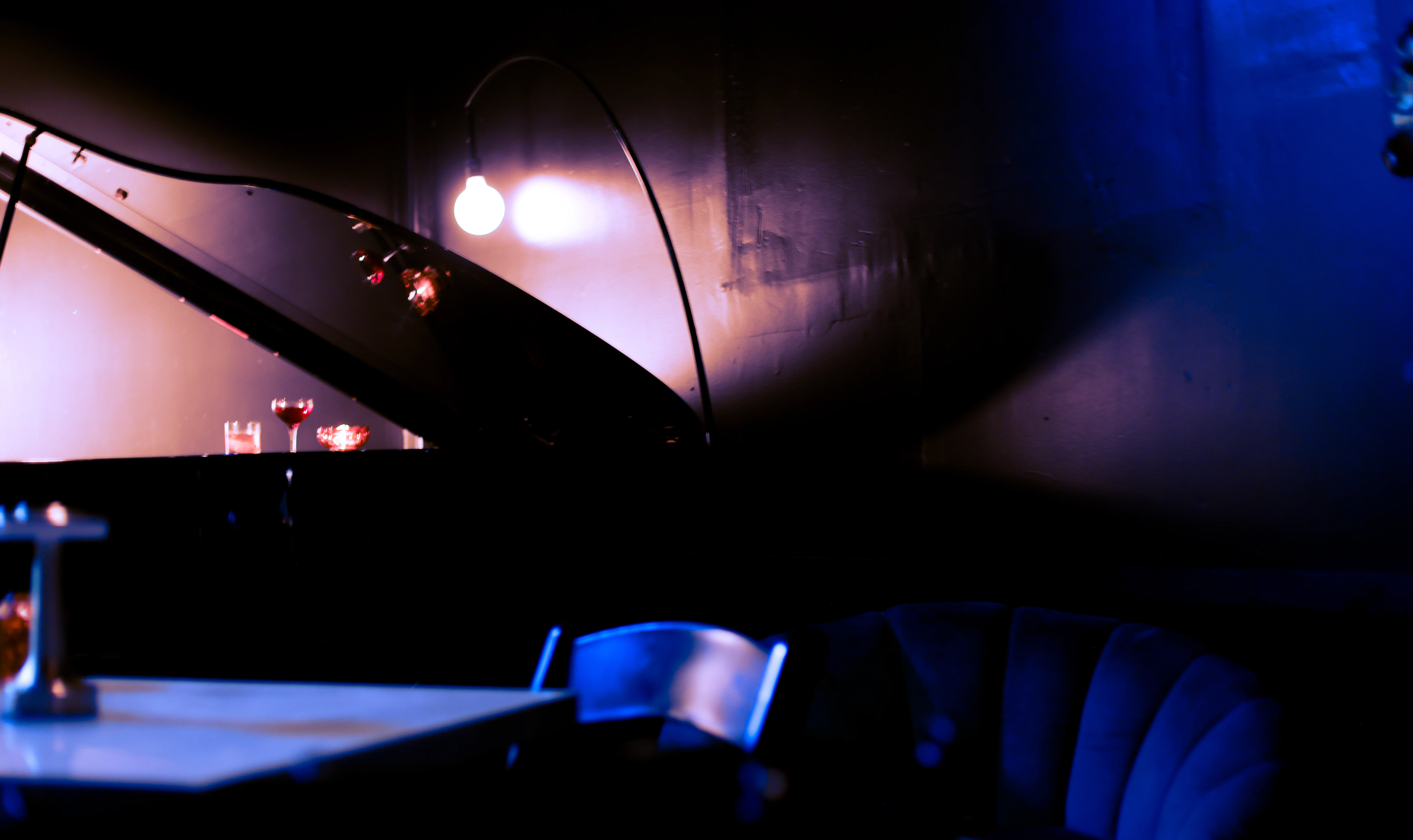 An interior view of a bar area with a dark wood counter, shelves of liquor, and hanging lights creating a cozy ambiance.