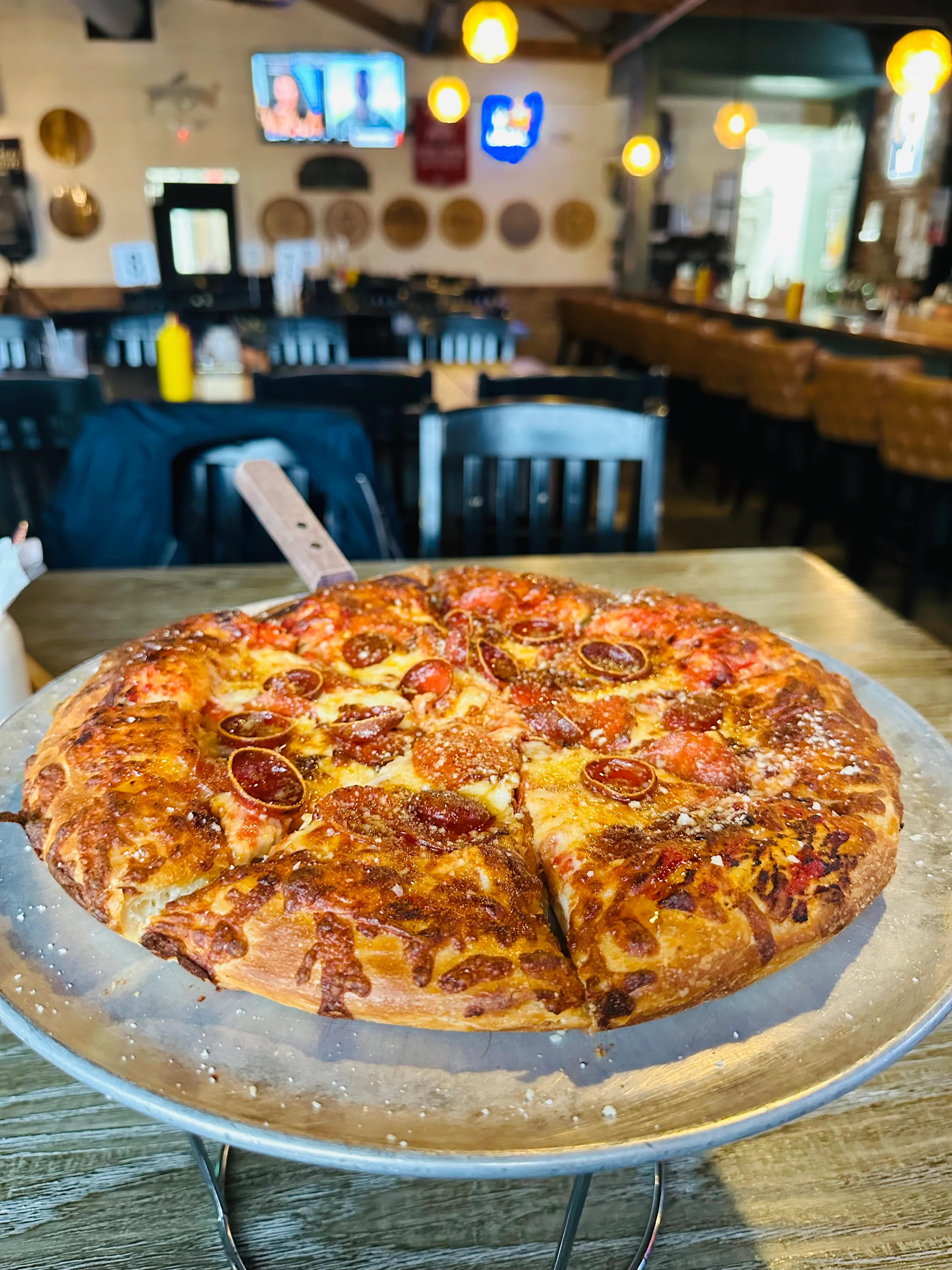 A freshly baked pizza topped with pepperoni and cheese, displayed on a metal serving tray in a casual dining setting.