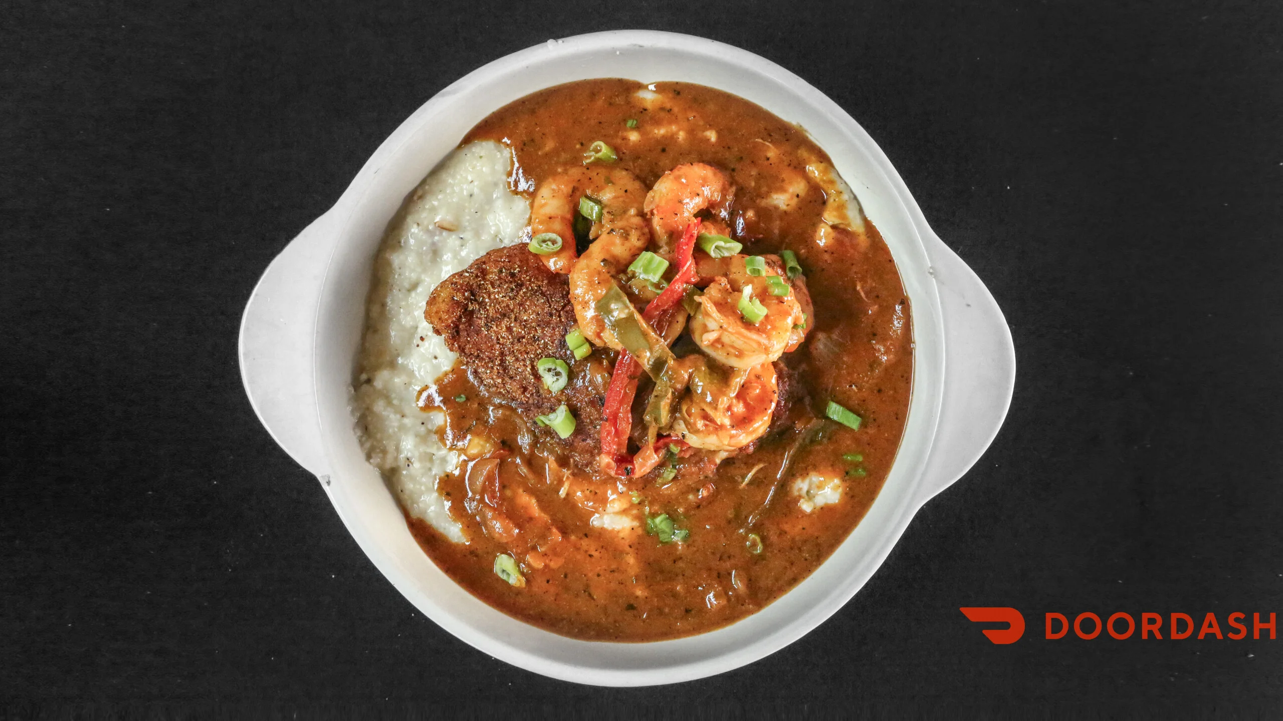 A bowl of shrimp and grits with a savory sauce, garnished with green onions and served with a fried cake.