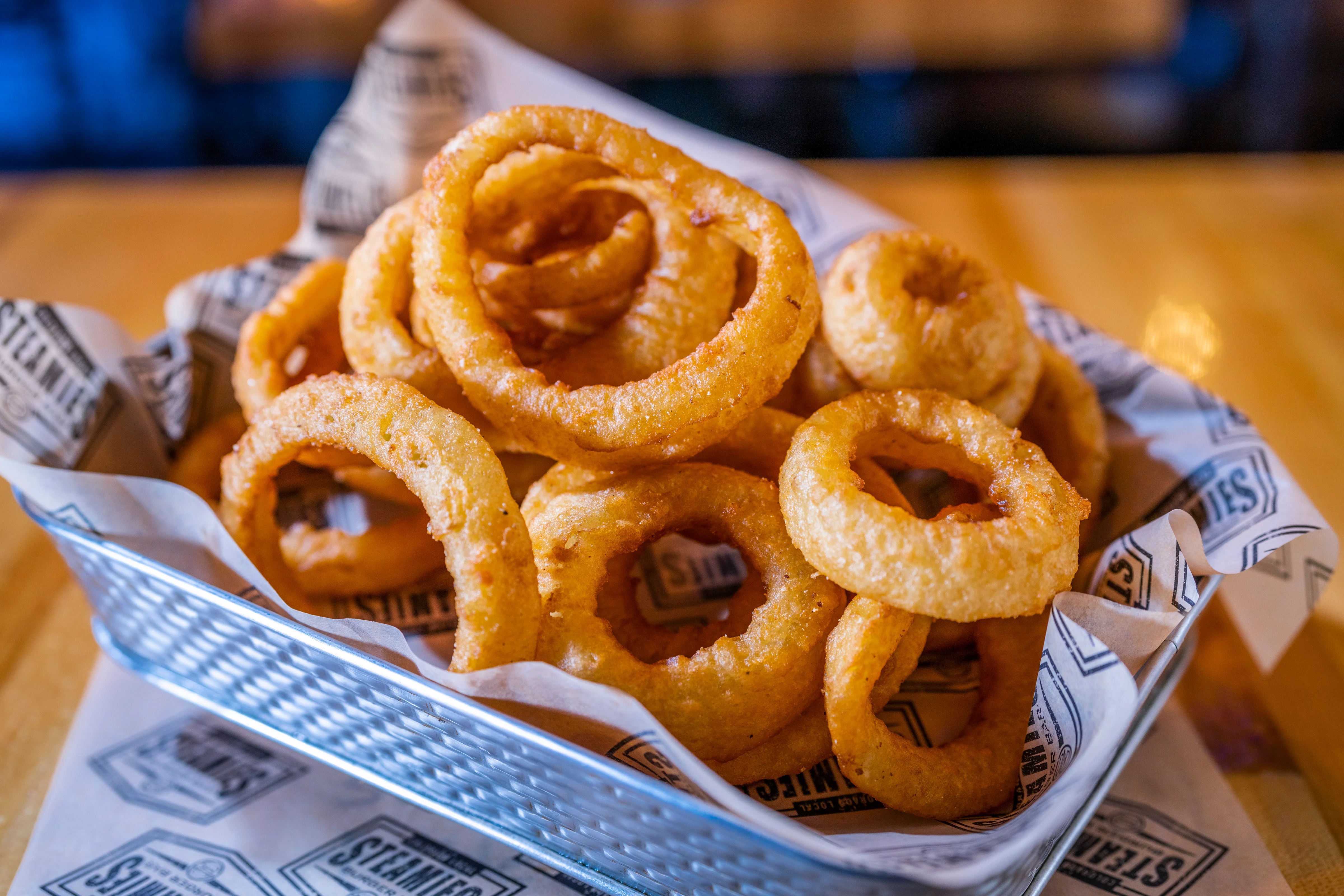 A serving of crispy onion rings piled in a metal basket lined with paper.