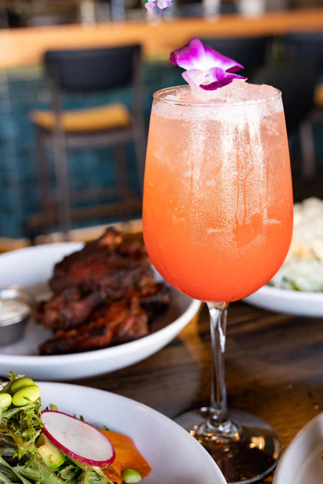 A refreshing pink cocktail garnished with a flower in a tall glass, accompanied by several plates of food.