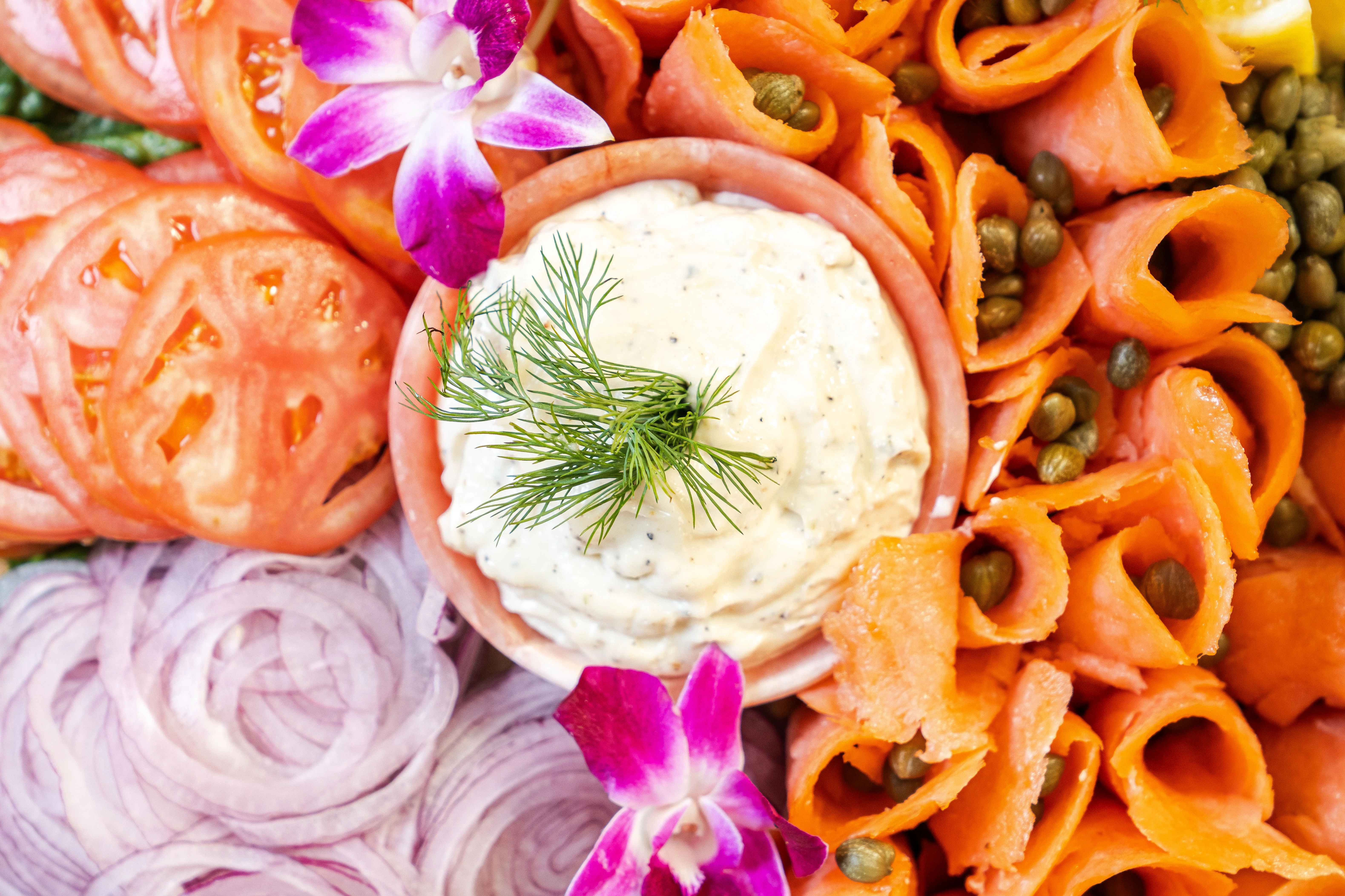 A platter with smoked salmon, tomatoes, onions, capers, and a creamy dip.