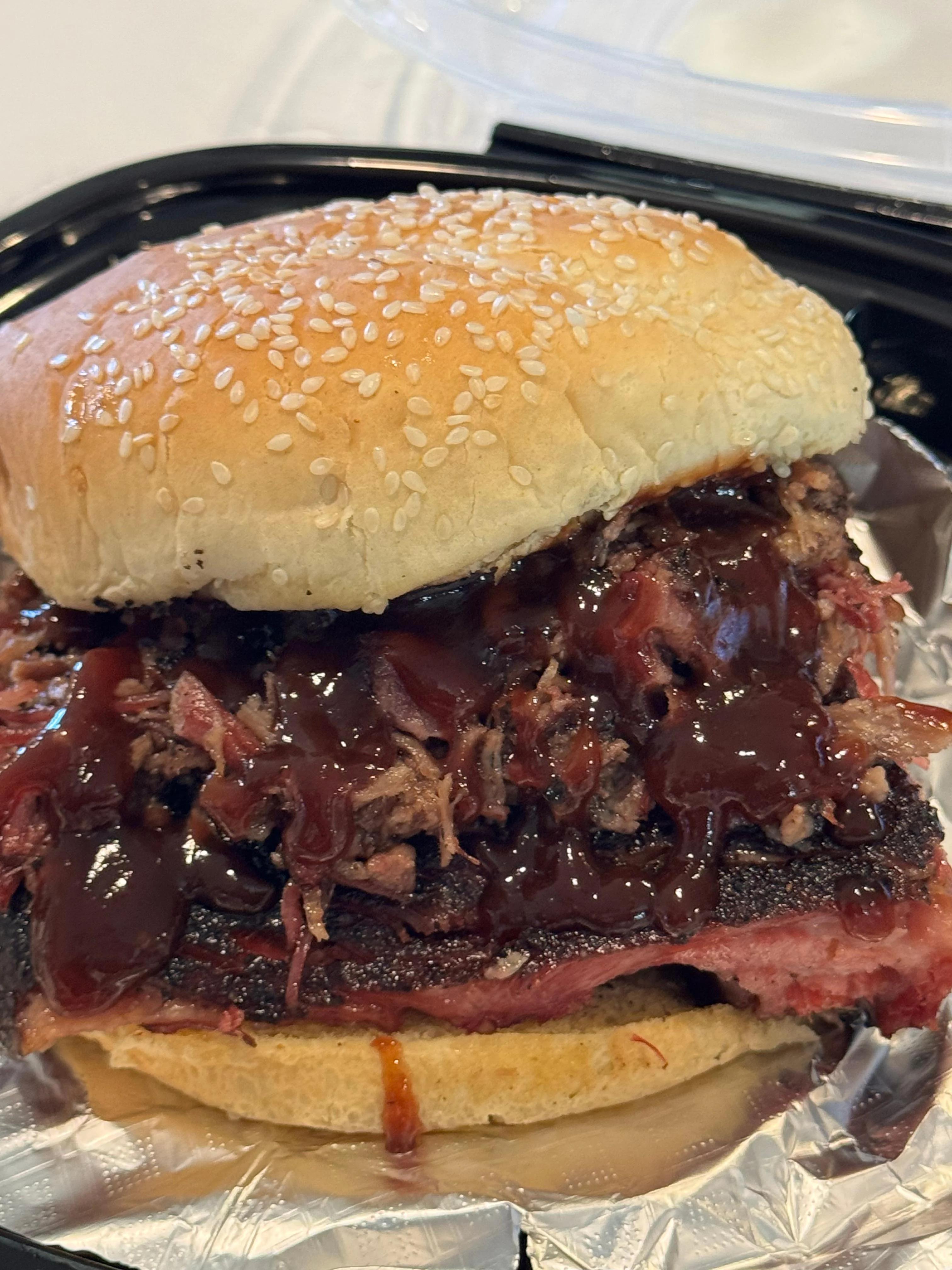 A hearty sandwich featuring a sesame seed bun filled with pulled meat coated in barbecue sauce.