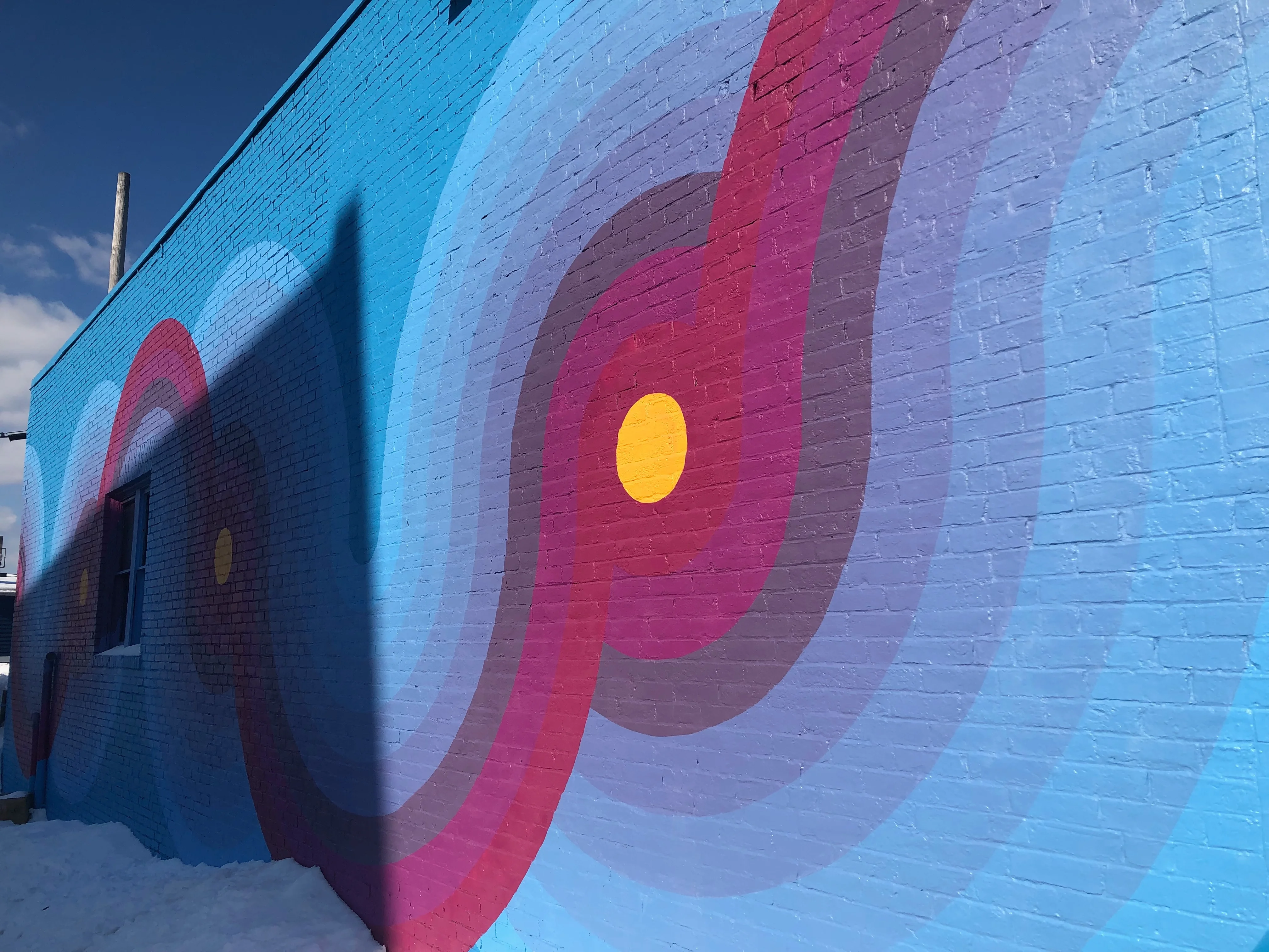Colorful mural on a brick wall with swirling patterns and a bright yellow circle