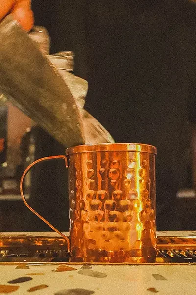 Bartender pouring drink into a copper mug at a bar.