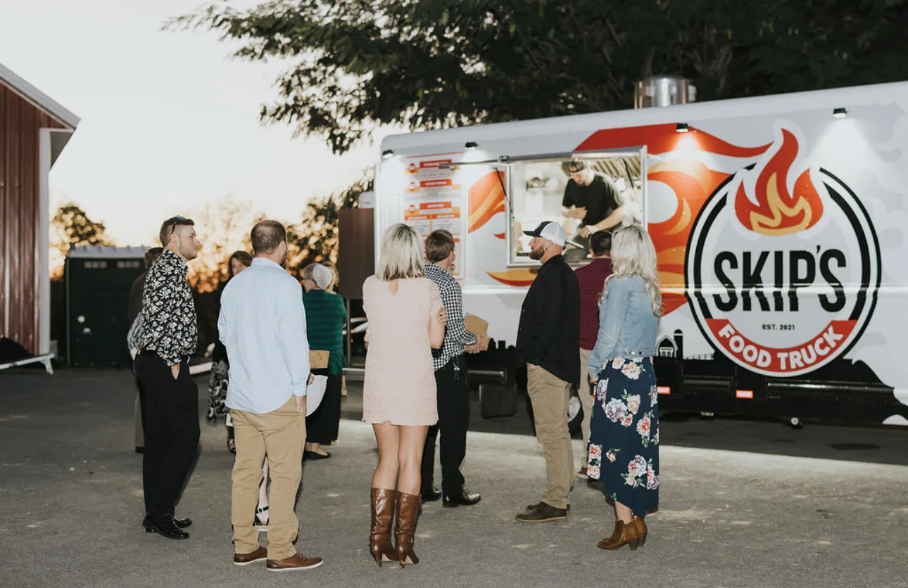 Guests enjoying food from a vibrant food truck at sunset