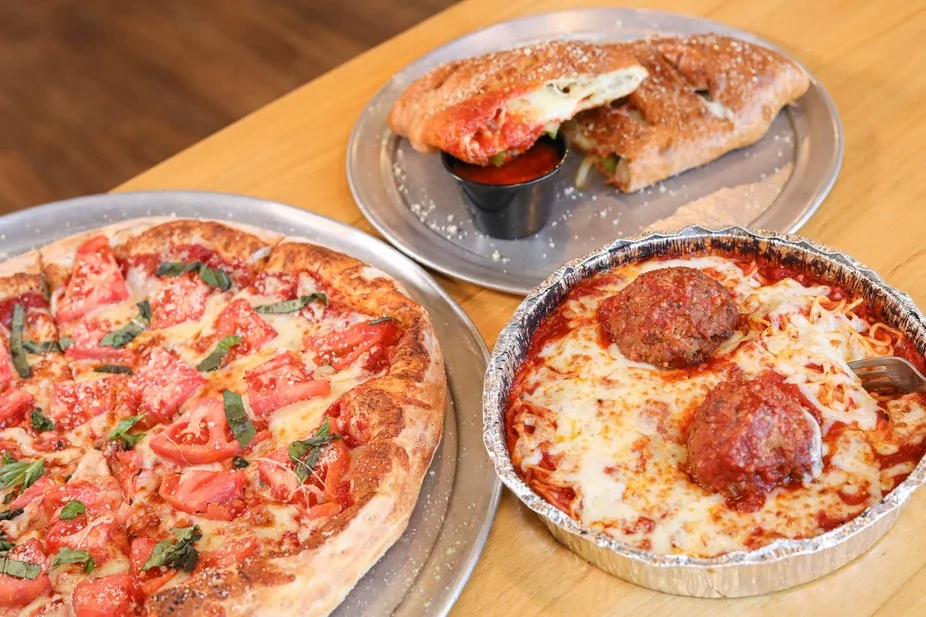 A meal featuring a thin-crust pizza topped with tomatoes and basil, a serving of meatballs in marinara sauce, and a calzone filled with cheese and toppings.