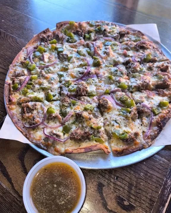 A freshly baked pizza topped with beef, green peppers, and red onions, served with a side of dipping sauce.