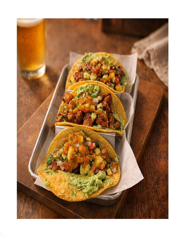 Three vibrant tacos with guacamole and toppings on a rustic tray