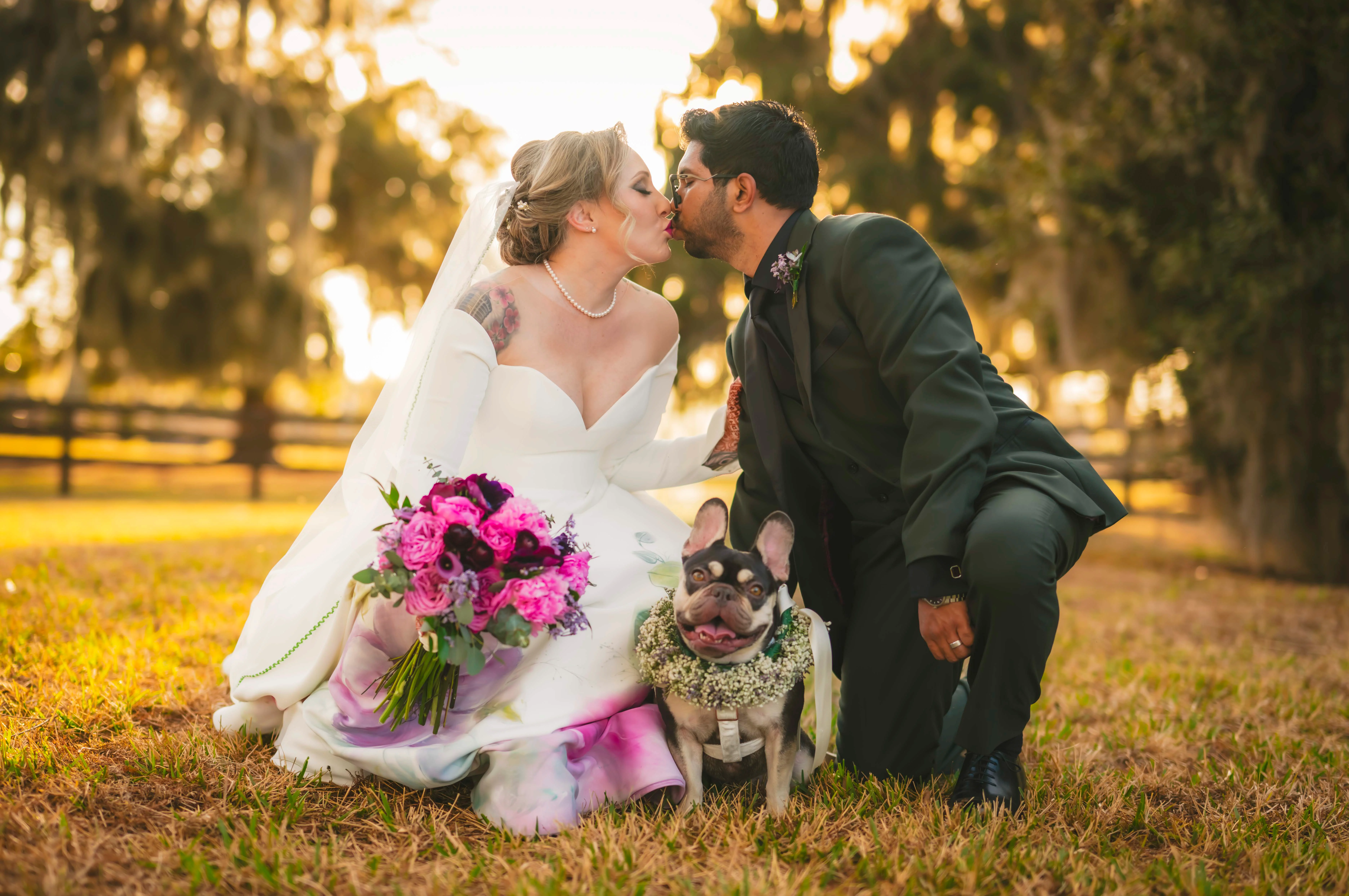 Bride and groom sharing a kiss with their dog in a scenic outdoor setting
