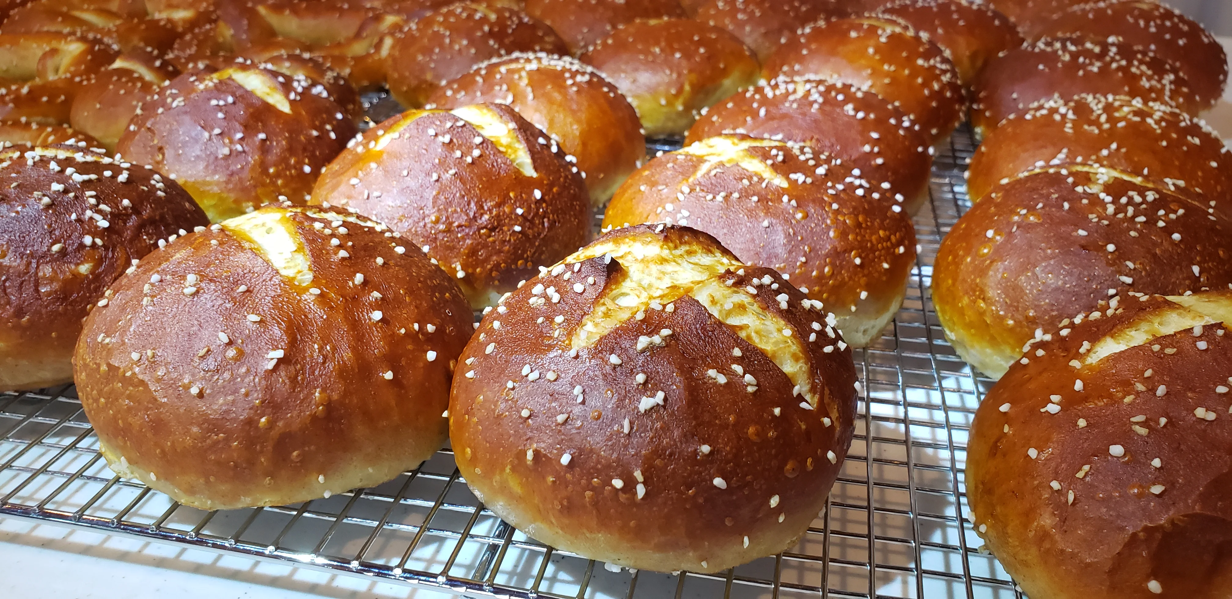 Freshly baked pretzel rolls with sesame seeds on a cooling rack.