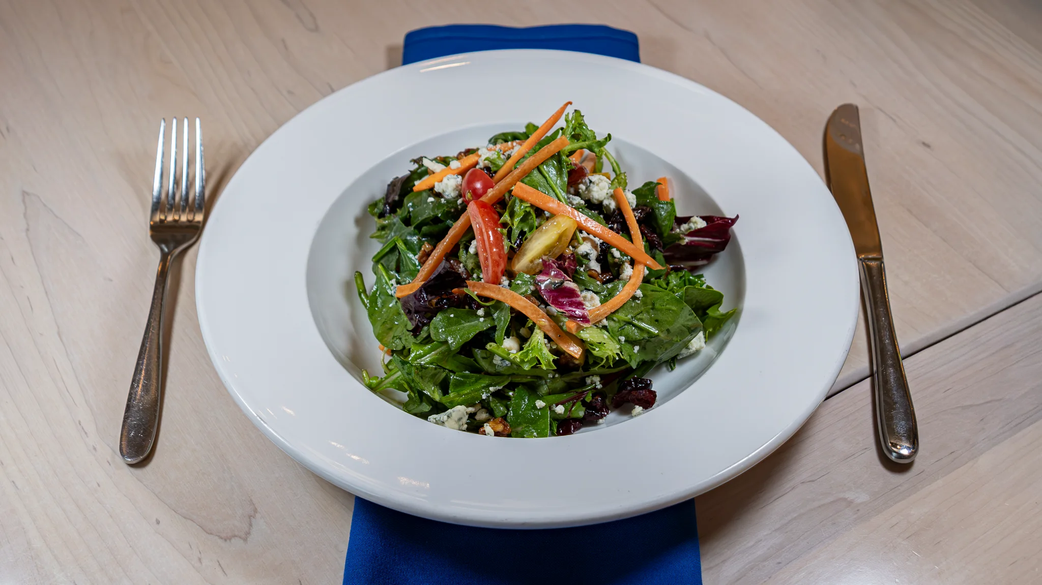 A fresh salad with grilled shrimp, mixed greens, and various toppings including radishes and pumpkin seeds served in a white bowl.