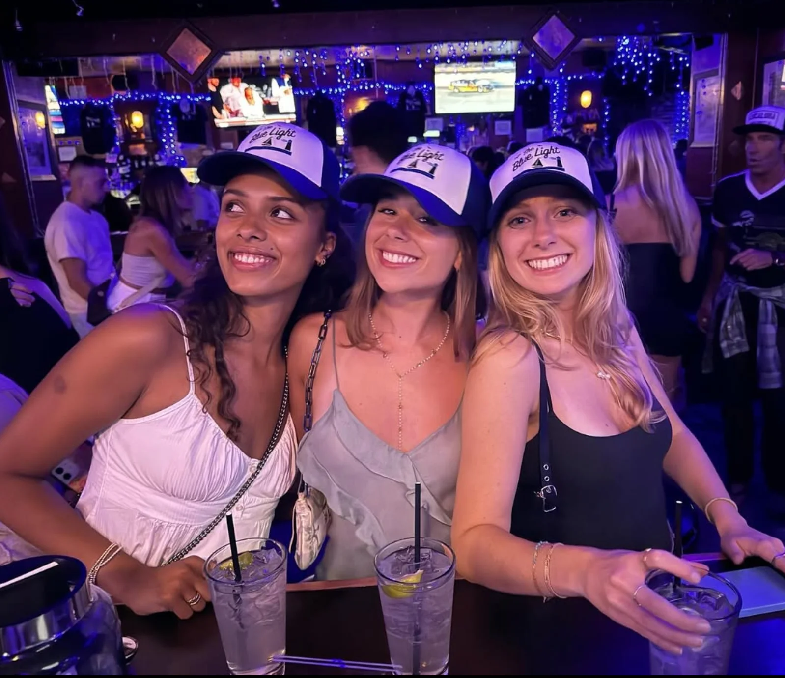 Three friends enjoying drinks at a lively bar with blue lighting