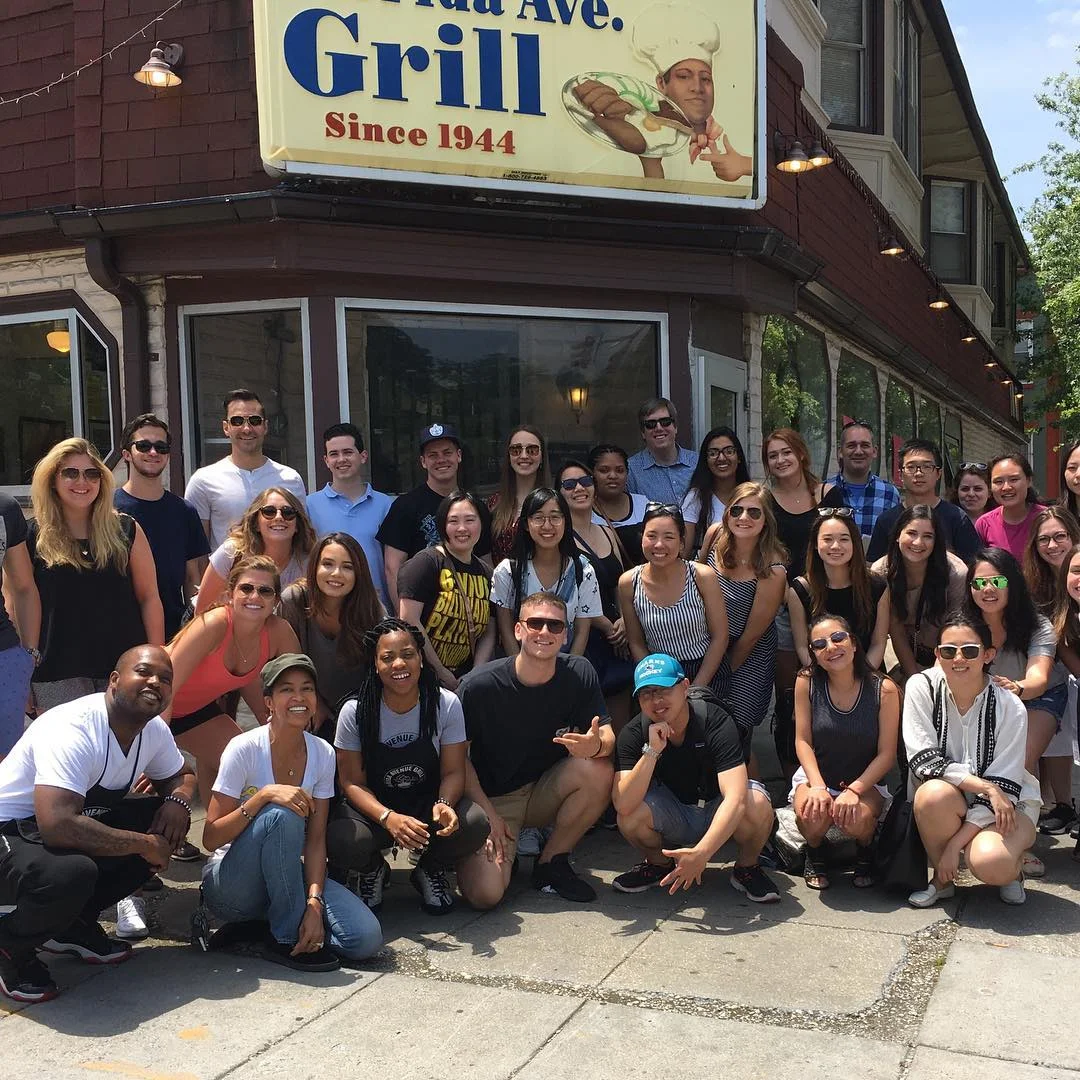Large restaurant group posing outside Avenue Grill storefront