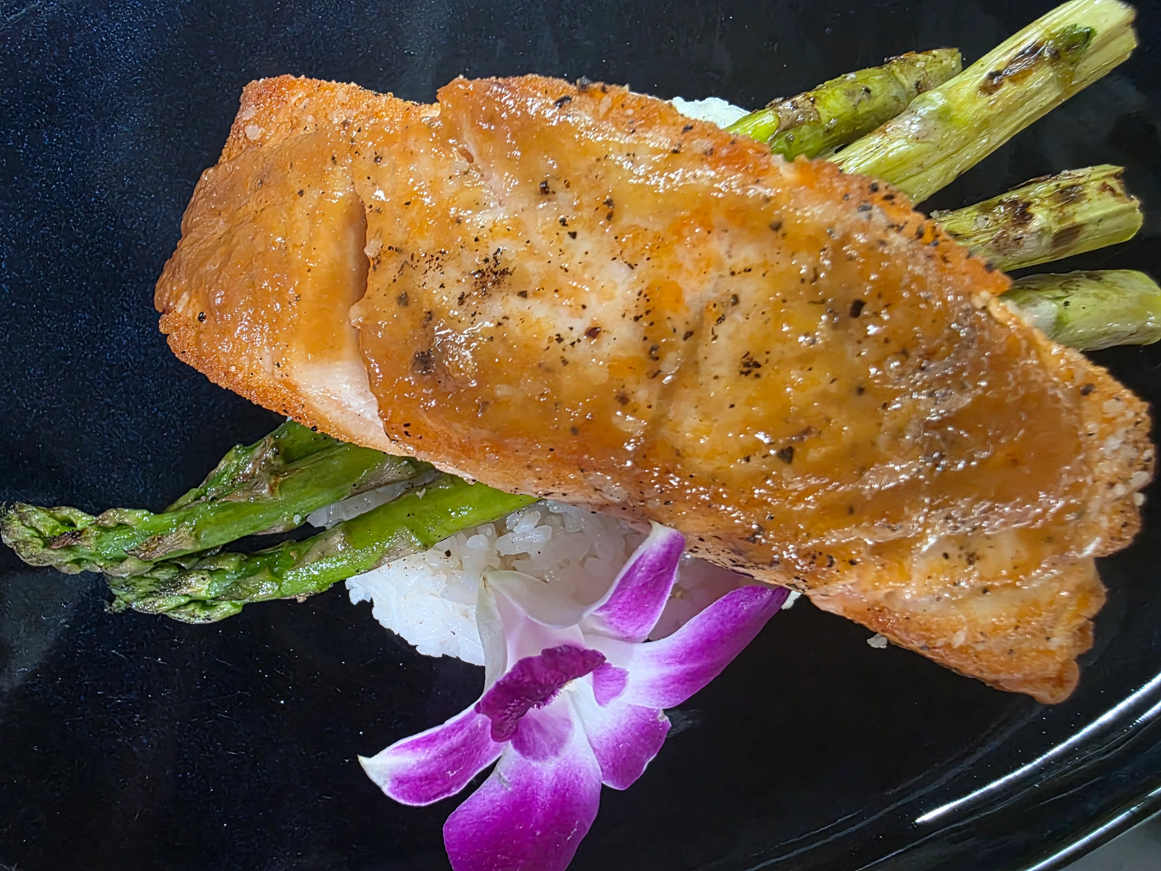 Pan-seared salmon with asparagus and rice, garnished with orchid flower