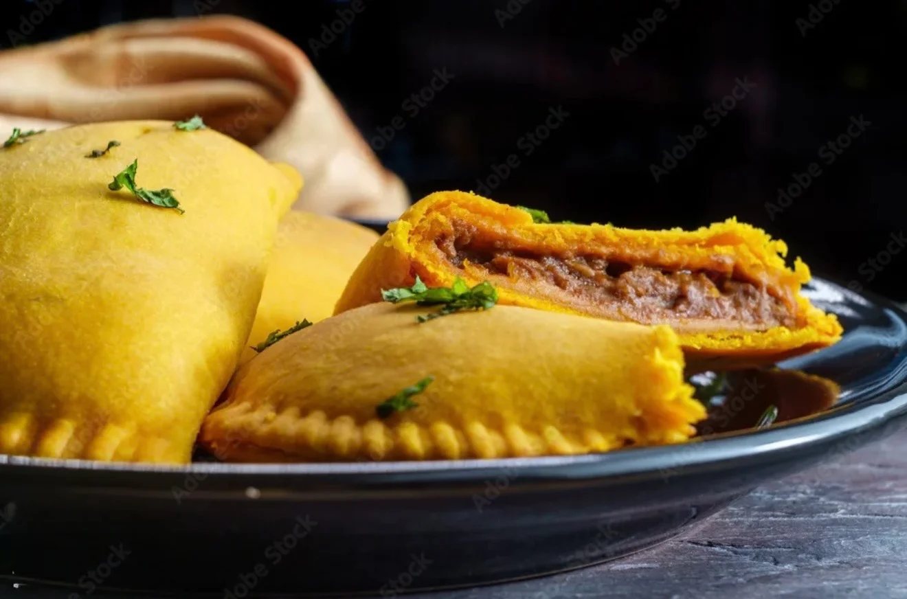 A plate of golden empanadas, some sliced open to reveal a savory filling, garnished with fresh herbs.