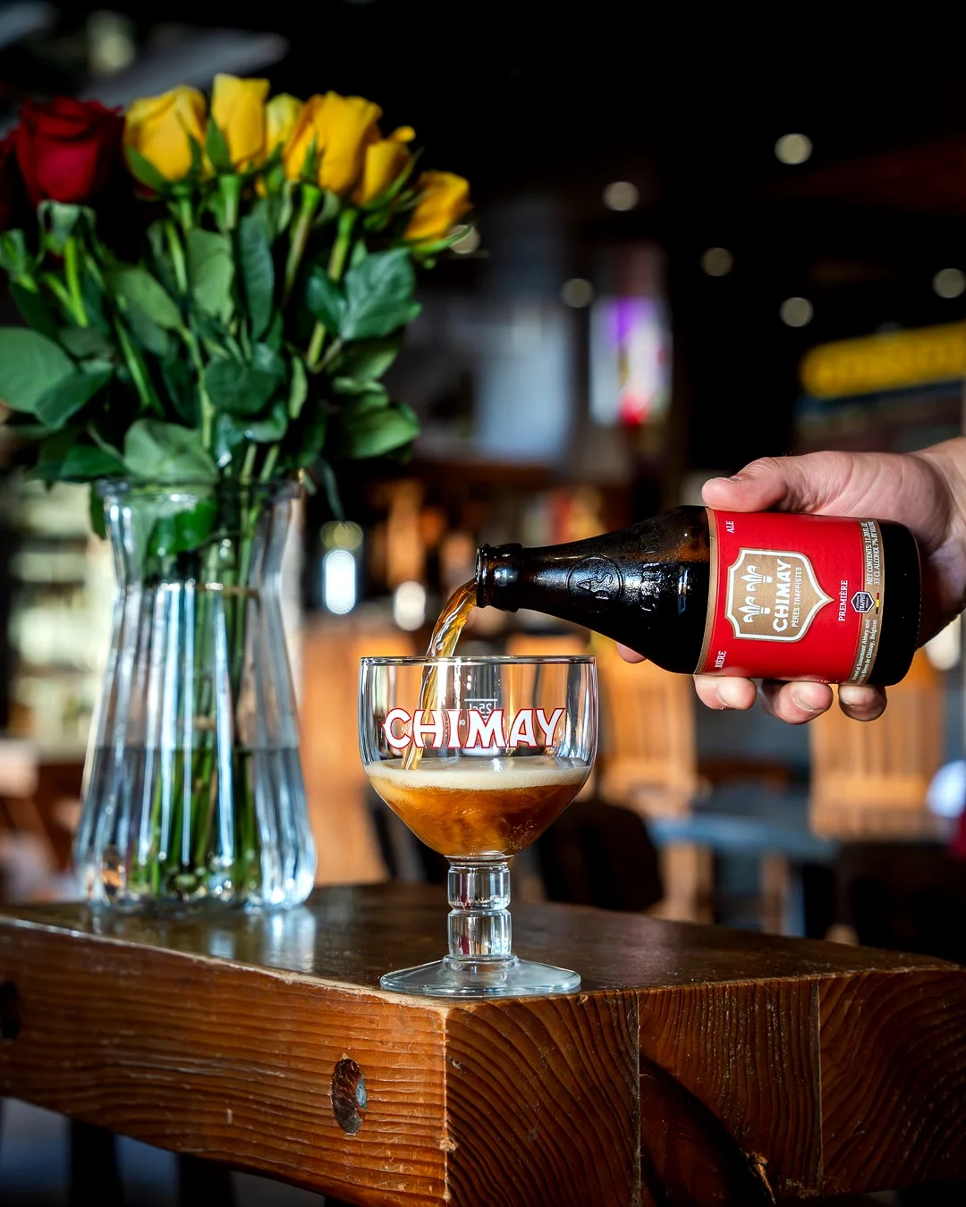 Pouring Chimay beer into a branded glass with a floral centerpiece.