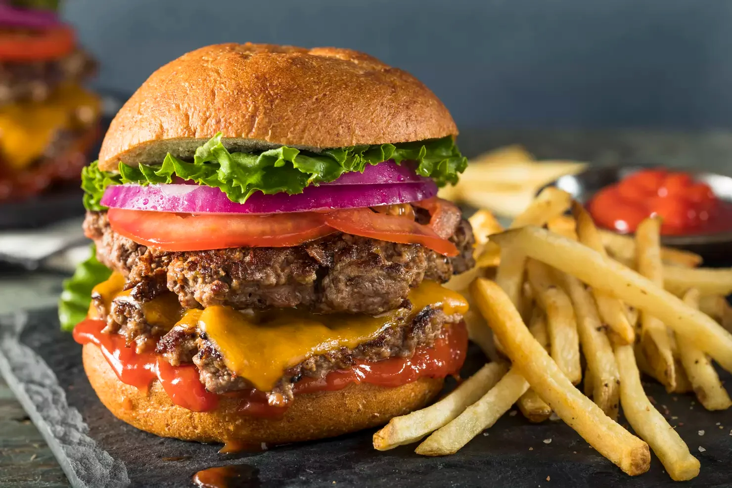 Juicy cheeseburger with fries on a rustic slate plate