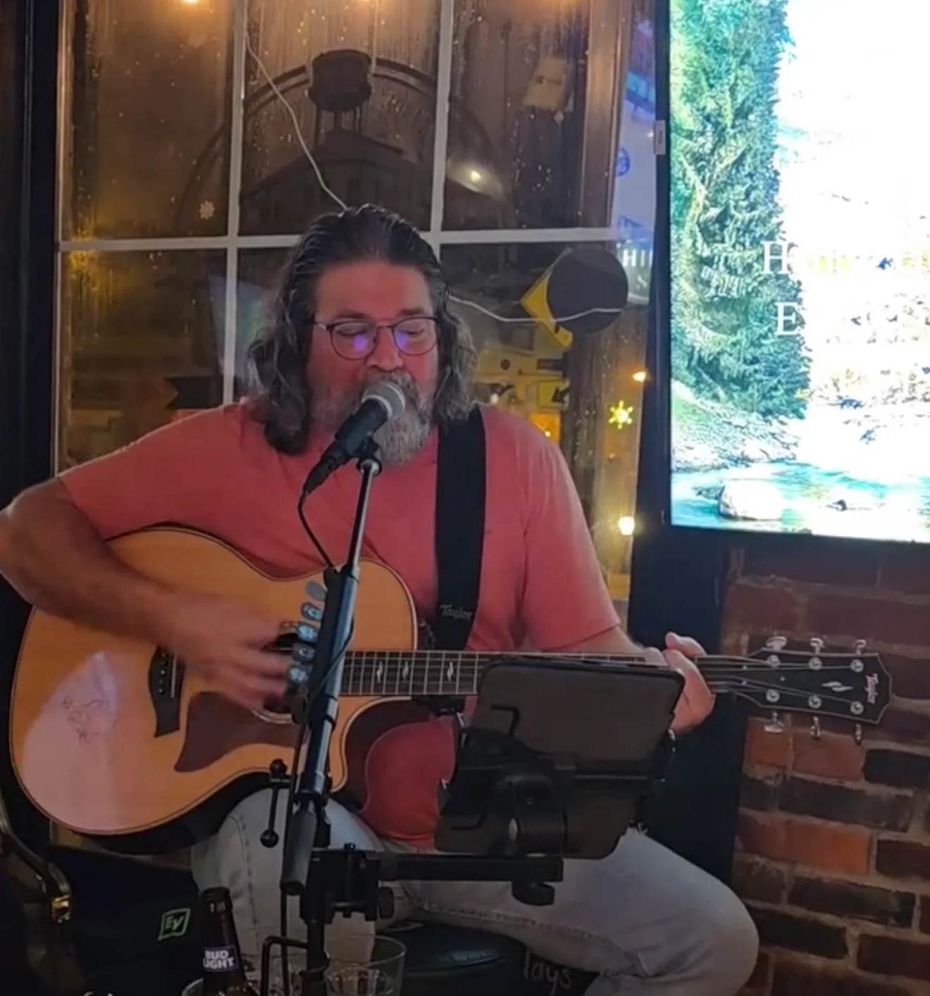 A man plays acoustic guitar and sings into a microphone, performing in a lively setting.