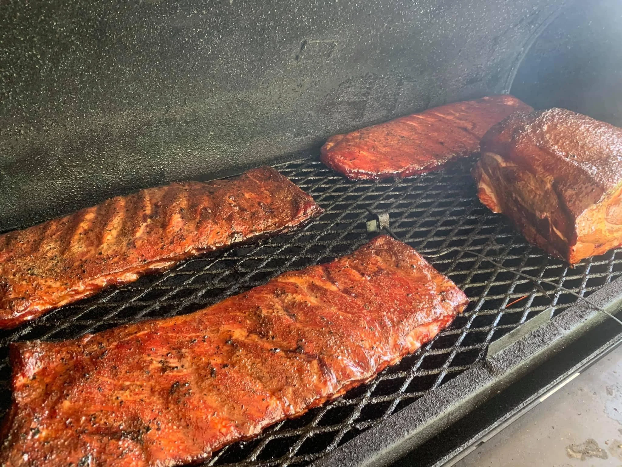 Several pieces of barbecued ribs and pork on a grill, showcasing a smoky exterior and rich color.