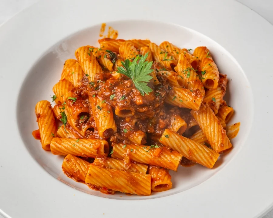 Plate of rigatoni pasta with rich red tomato sauce, garnished with fresh herbs, served on a white plate 