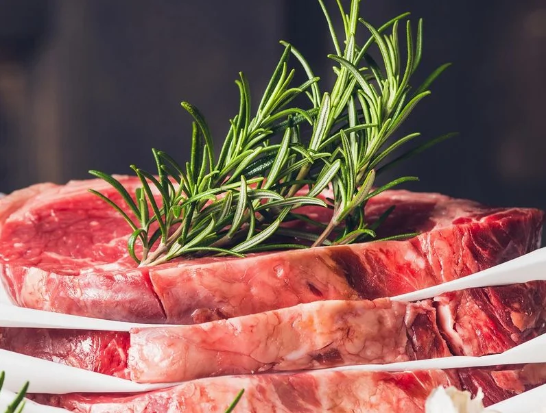 Raw ribeye steaks with rosemary, ready for grilling