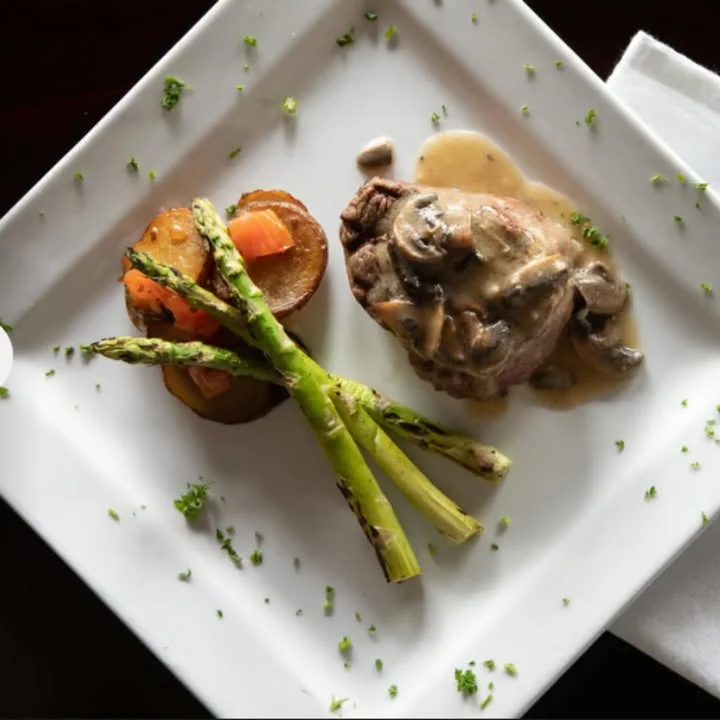 A gourmet dish featuring a steak with mushroom sauce, asparagus, and roasted potatoes.