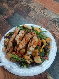 A fresh salad topped with grilled chicken strips, leafy greens, and croutons, served on a white plate.