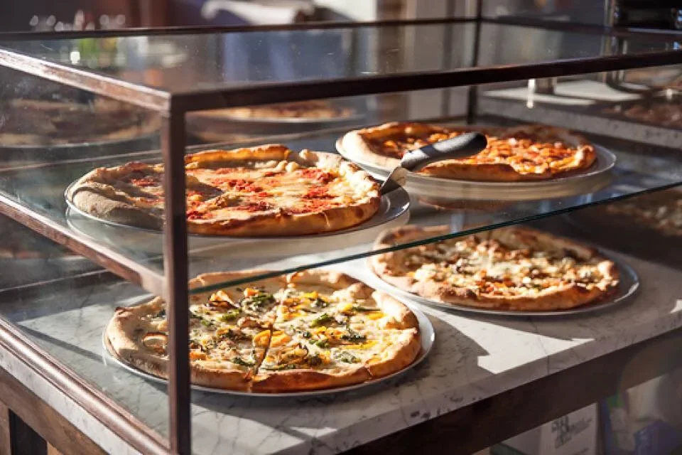 Assorted pizzas displayed in a glass case at a pizzeria