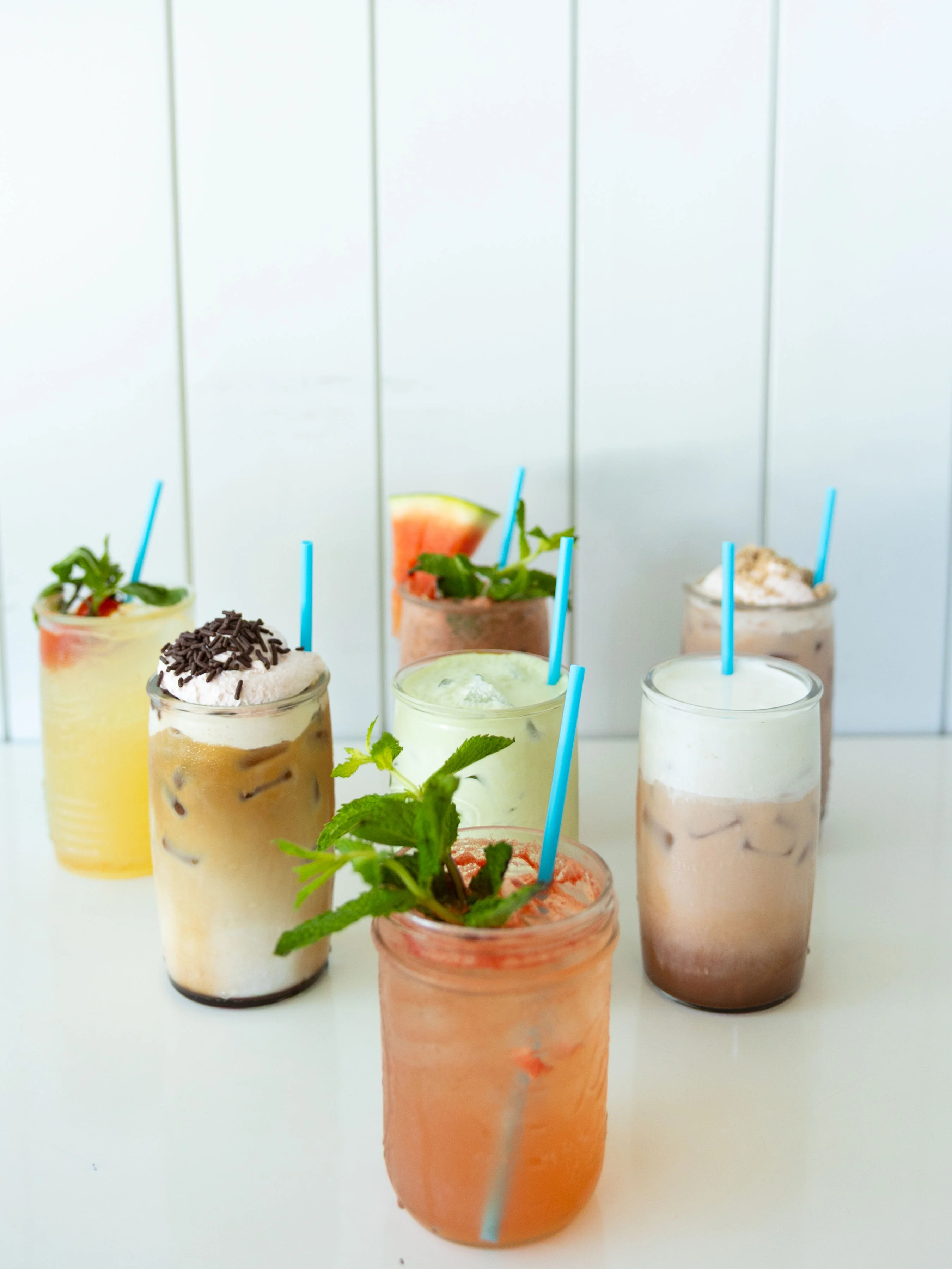 A variety of colorful drinks served in jars. Each drink has a different garnish and a bright straw.