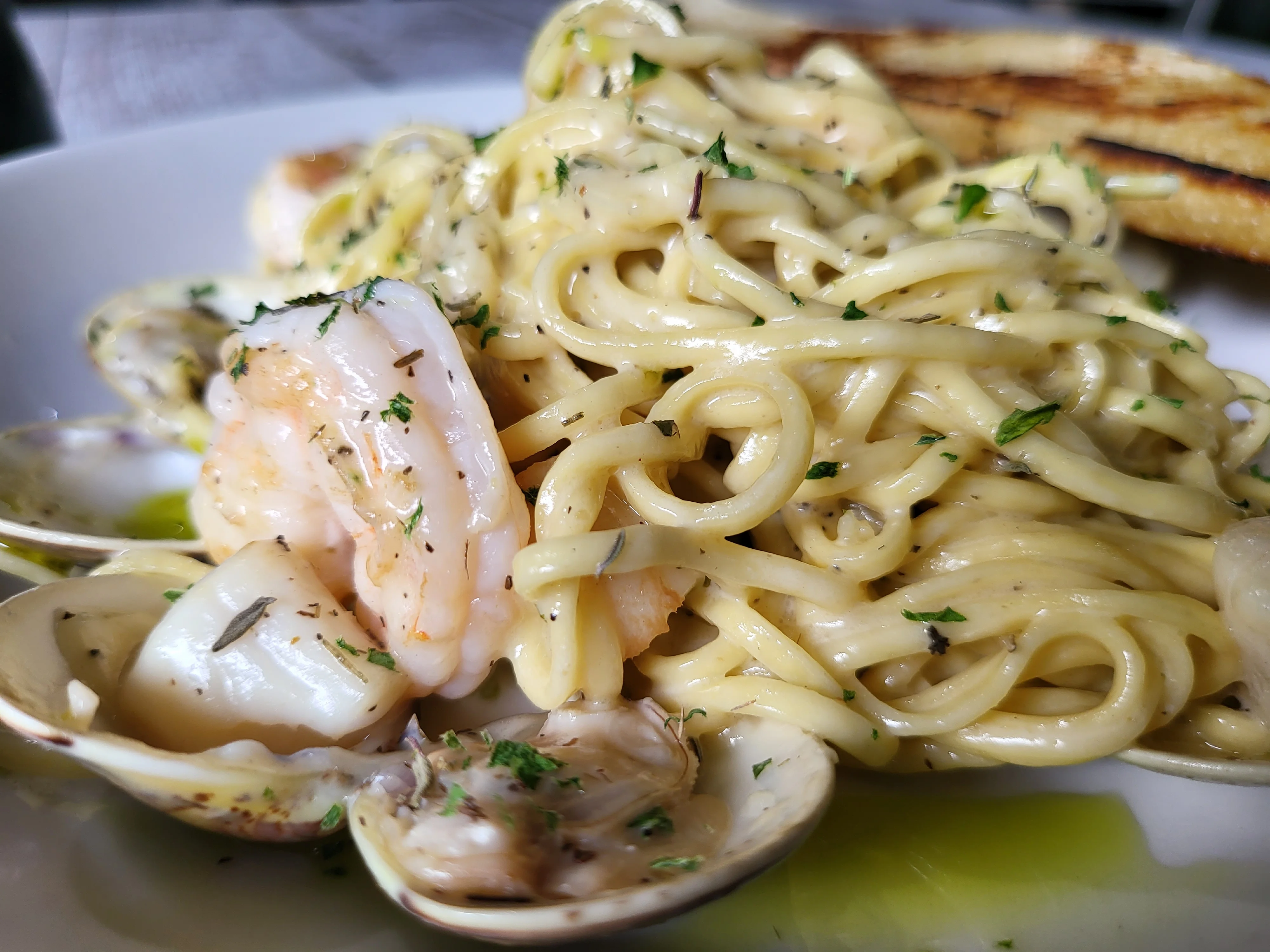 Seafood pasta with shrimp, clams, and creamy sauce garnished with herbs on a white plate.