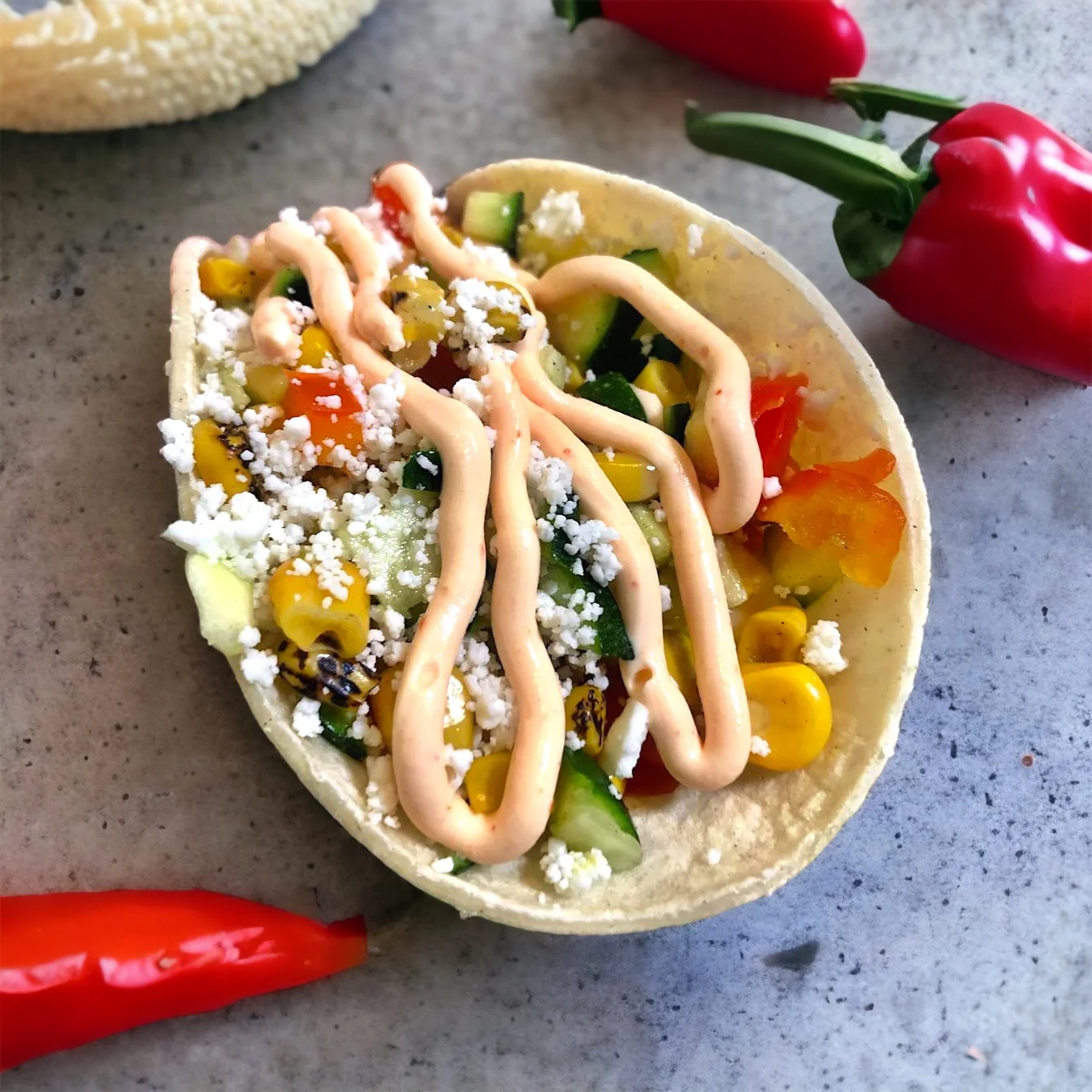 A taco shell filled with fresh vegetables, cheese, and a creamy sauce, garnished with chili peppers.