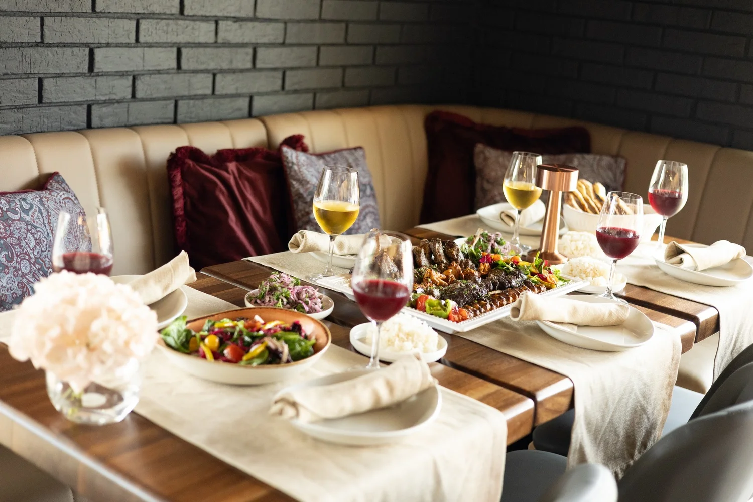 A beautifully set dining table featuring assorted grilled meats, salads, rice, and wine, creating an inviting atmosphere.