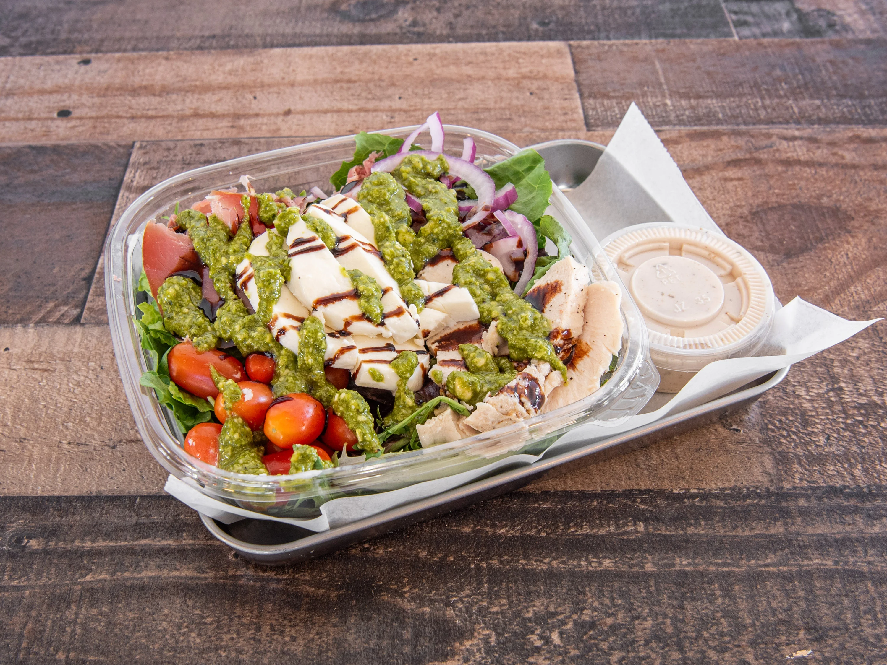 Grilled chicken salad with pesto dressing in a takeout container